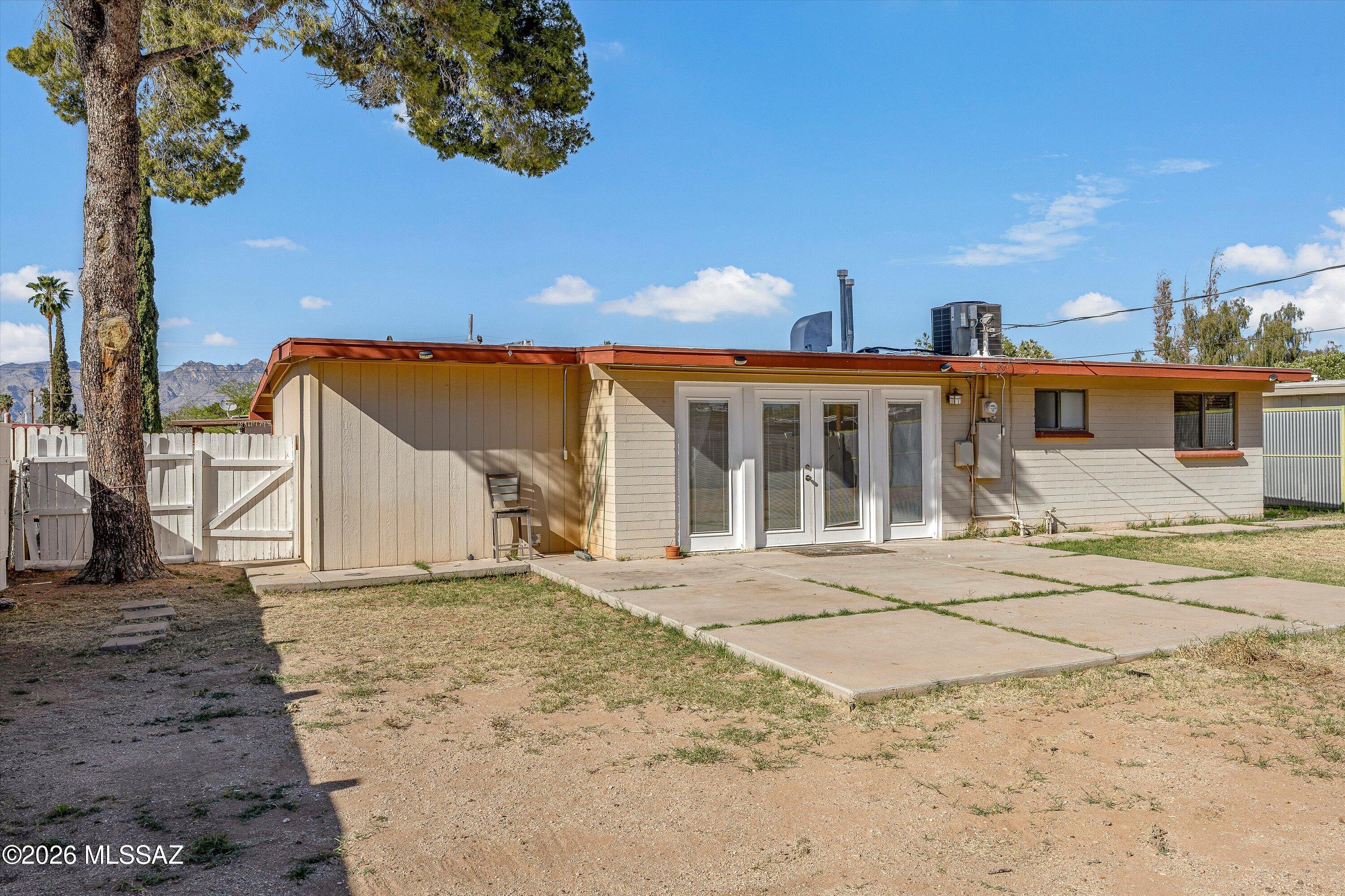 Single-story home with white French doors opening onto a concrete patio, with mountains in the distance.