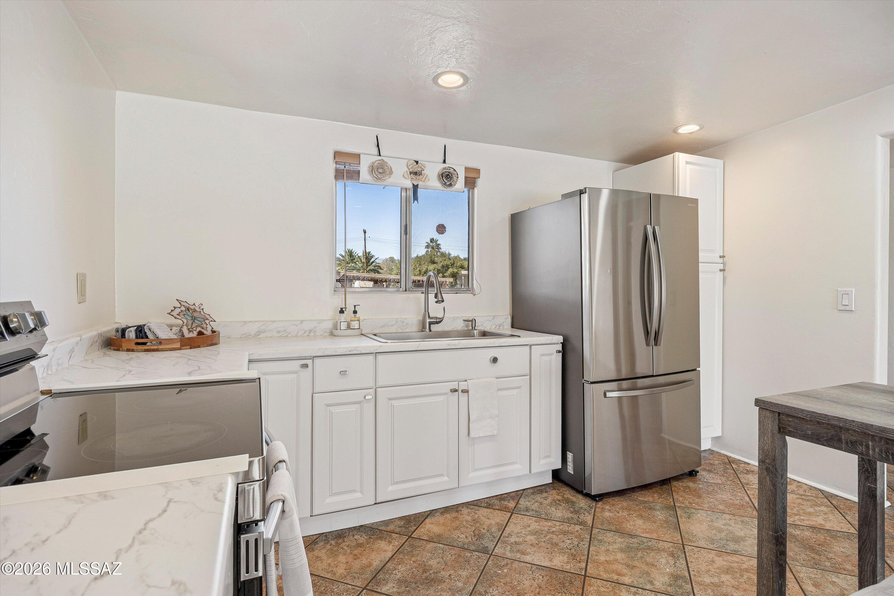 Kitchen with white cabinets, marble-look counters, stainless steel appliances, and a window above the sink.