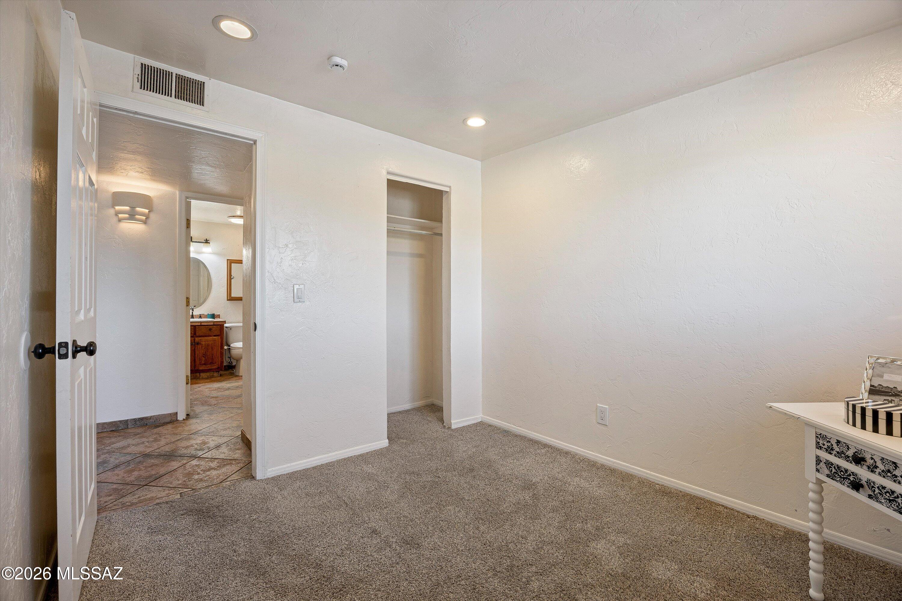 Carpeted bedroom with an open closet and doorway to a tiled bathroom.