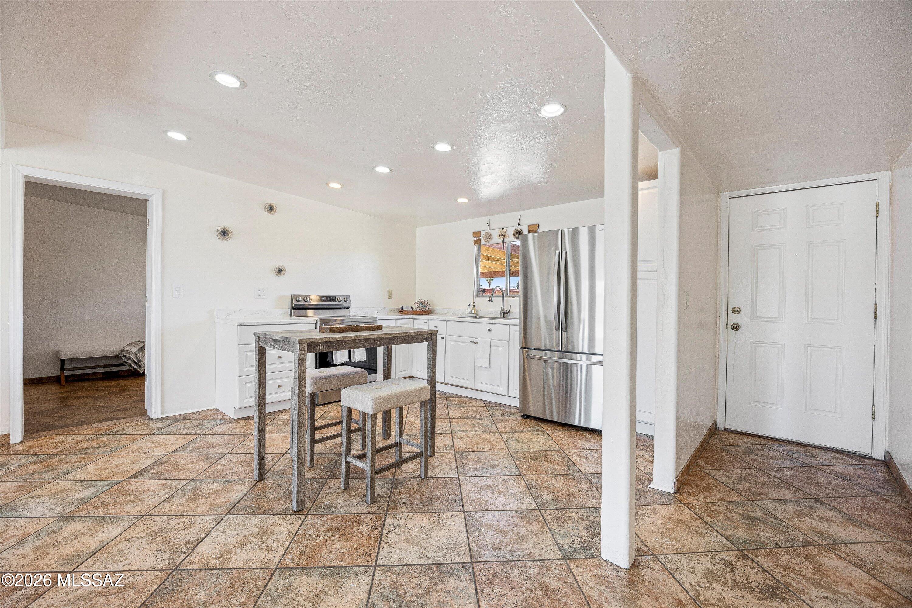 Kitchen with white cabinetry, stainless steel appliances, a small island table, and tan tile flooring.