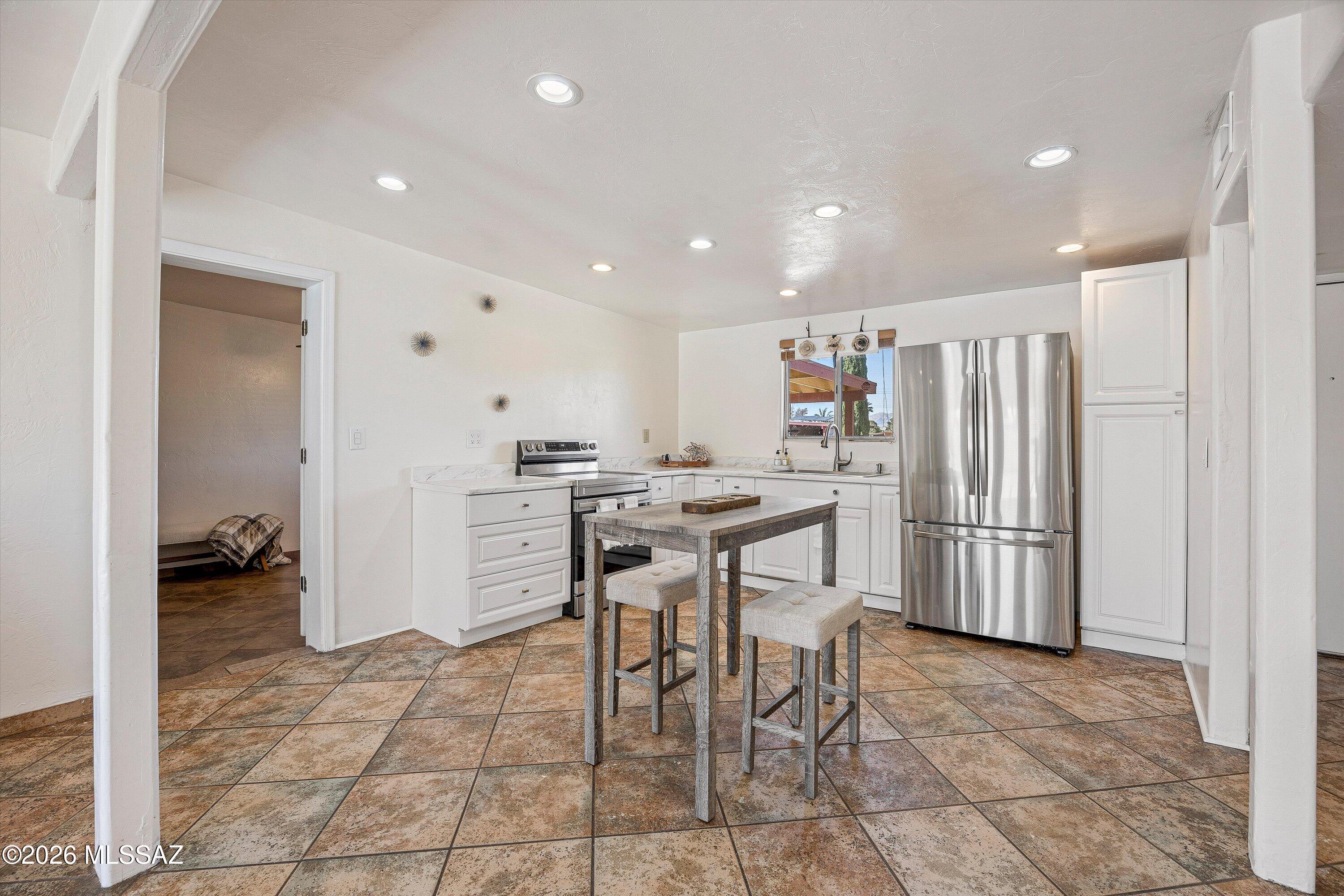 Kitchen with white cabinetry, stainless steel appliances, patterned tile floors, and a small table with stools.