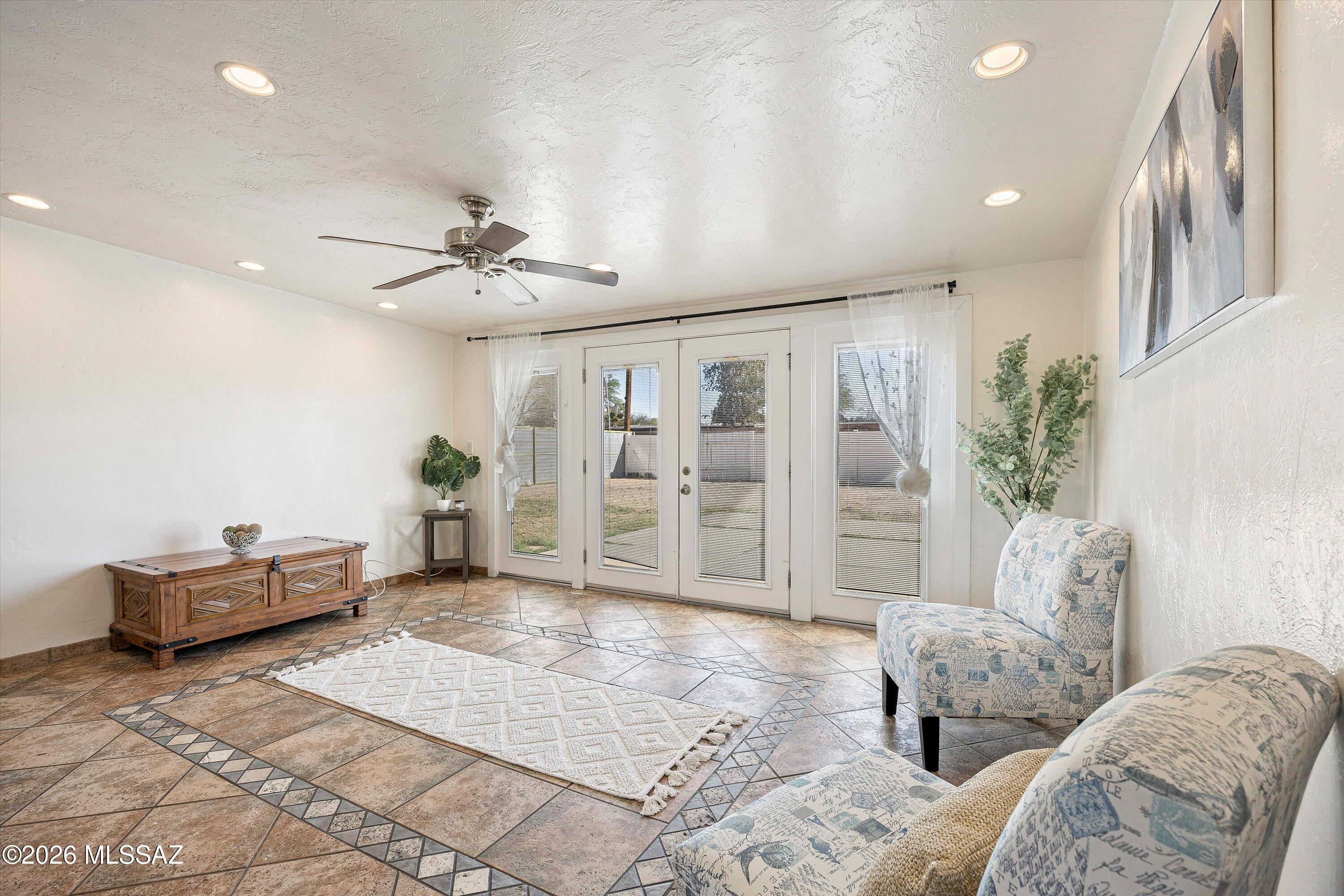 Living room with patterned chairs, tiled floors, and French doors overlooking a fenced yard.