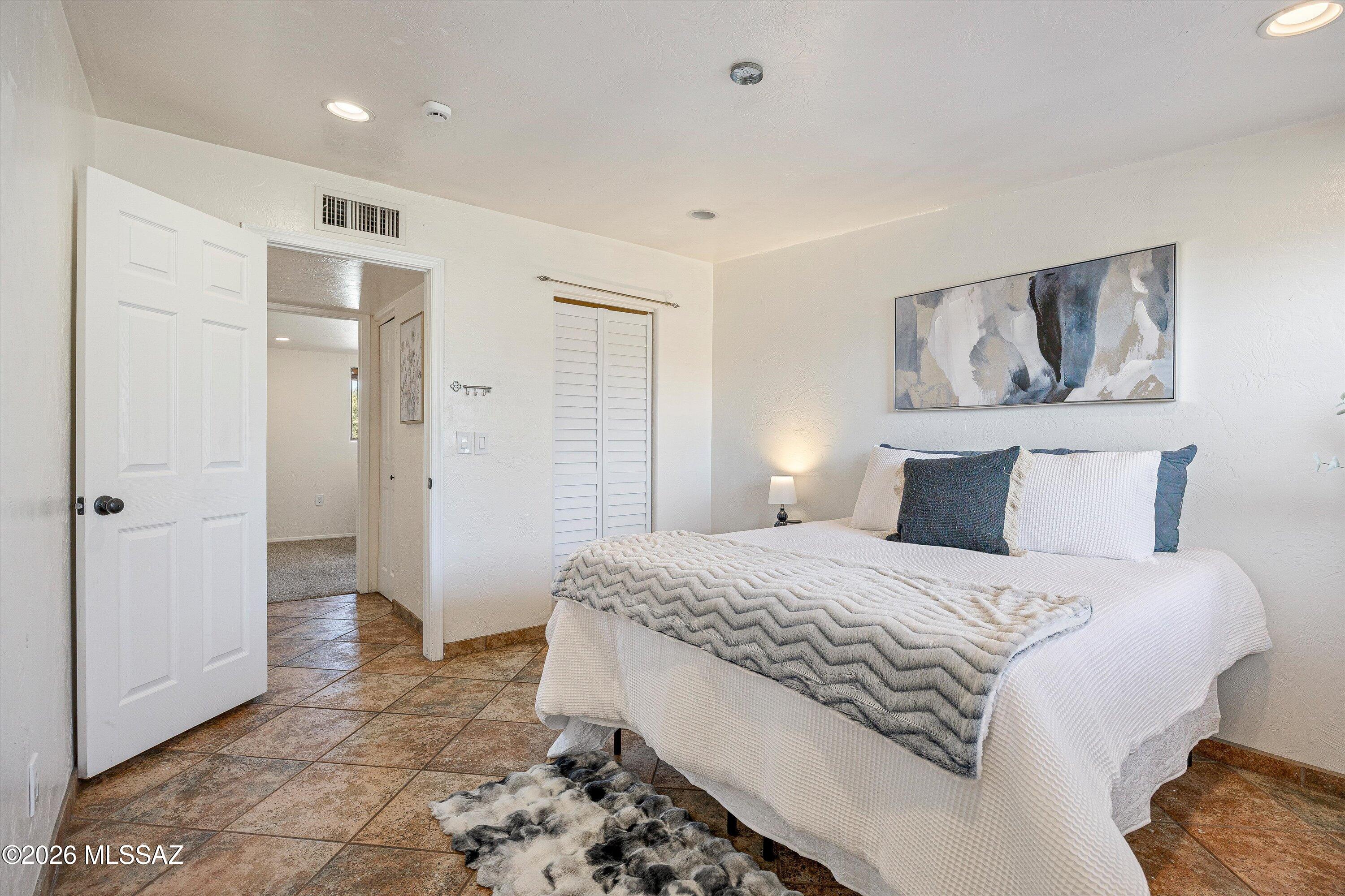 Furnished bedroom with a white bed, gray chevron blanket, blue pillows, and warm-toned tile floor.