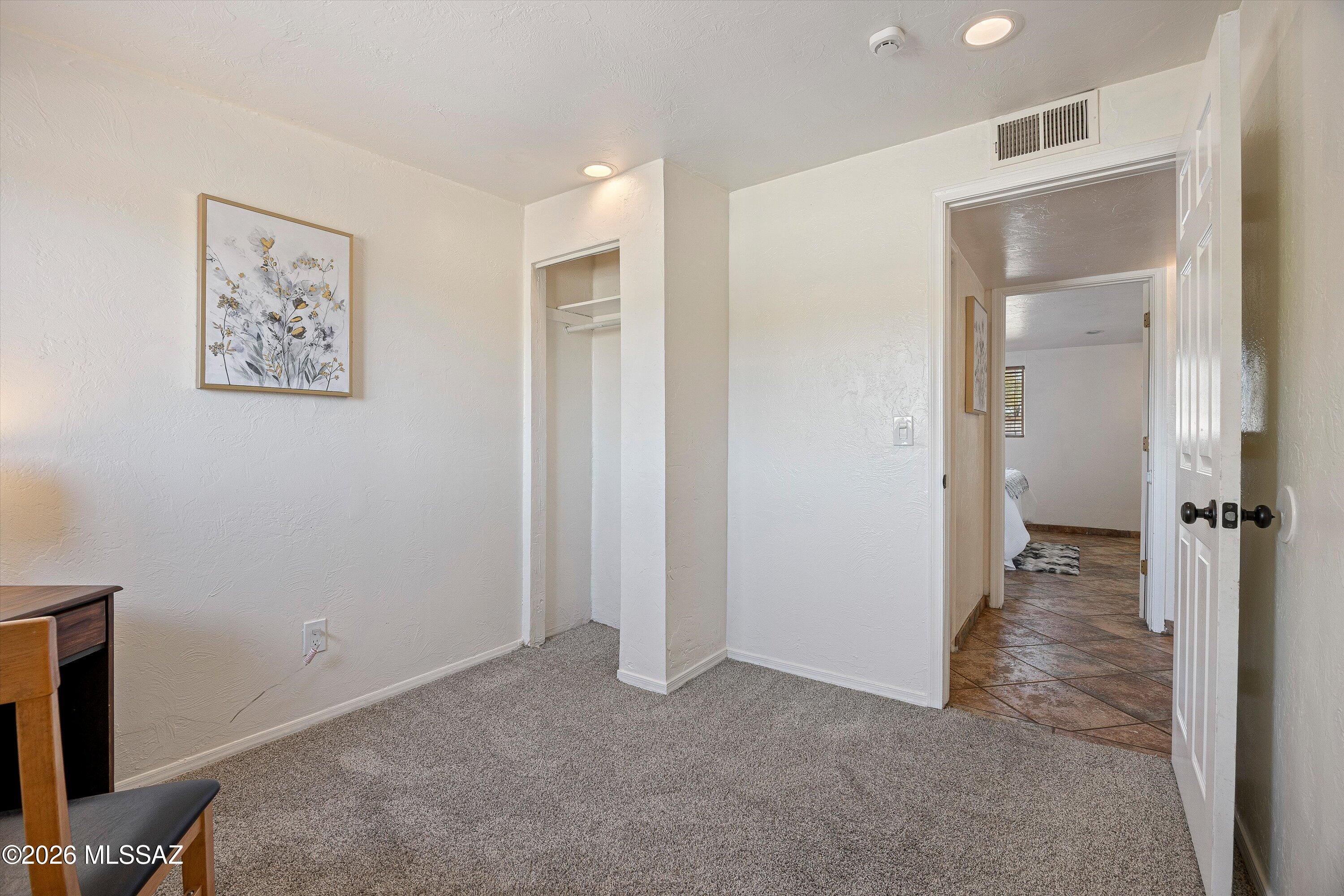 Carpeted room with an open closet and doorway leading to a tiled hall and bedroom.