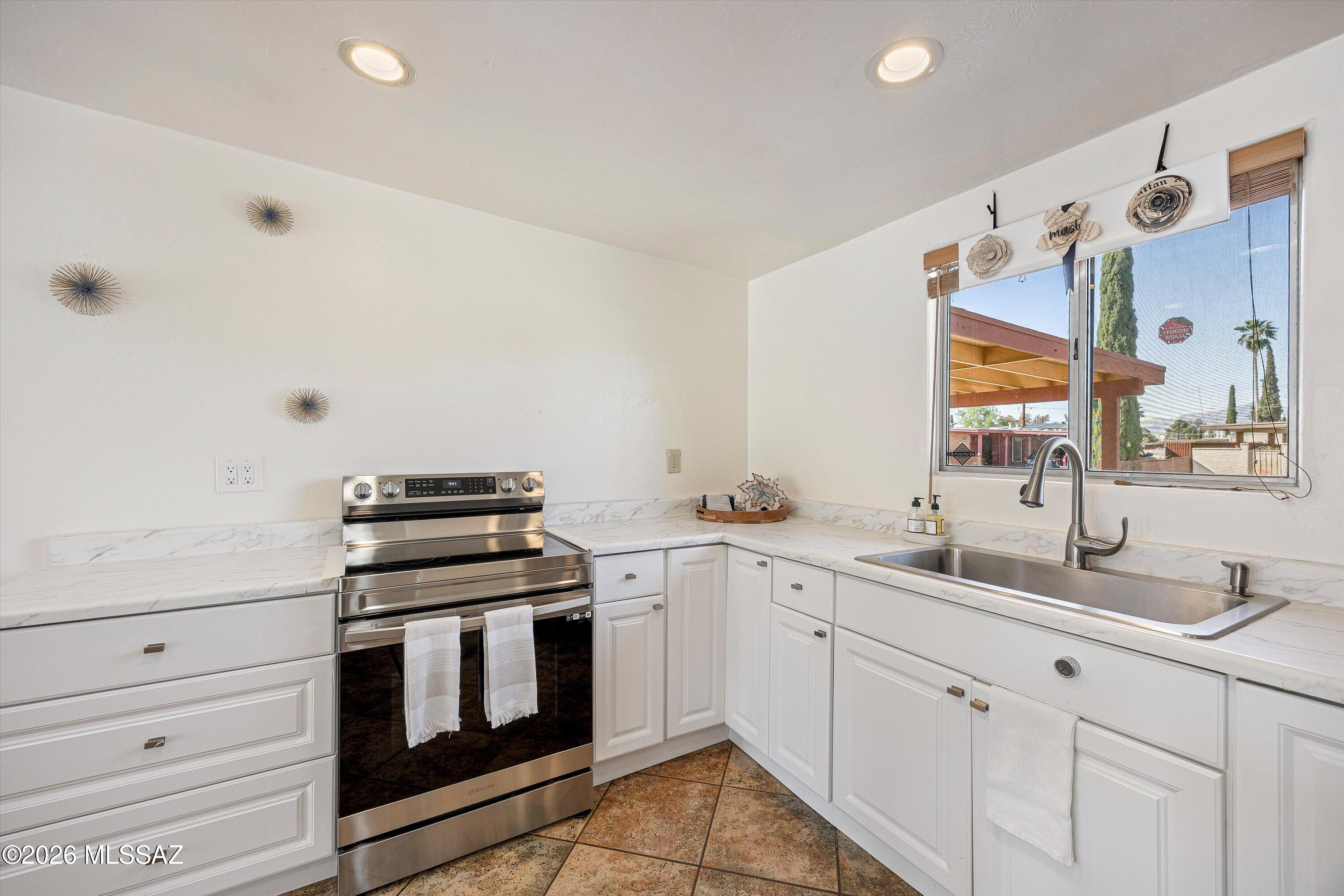 Bright white kitchen with stainless steel range, marble-look counters, and a large window above the sink.