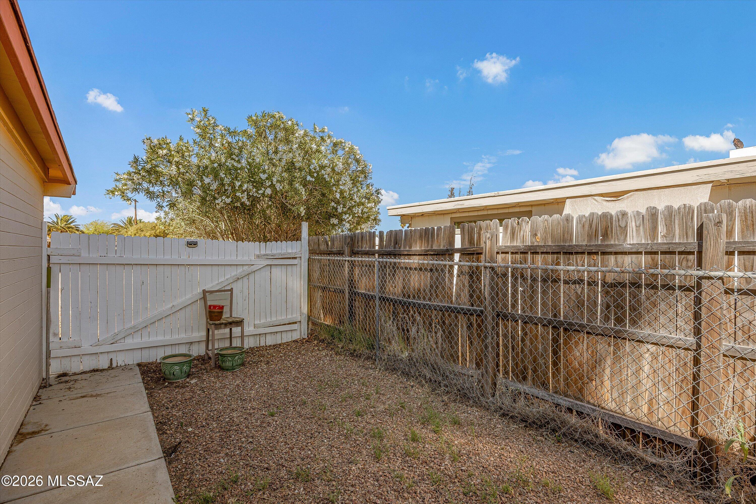 Fenced gravel backyard with a flowering tree, white gate, and chain-link fence.
