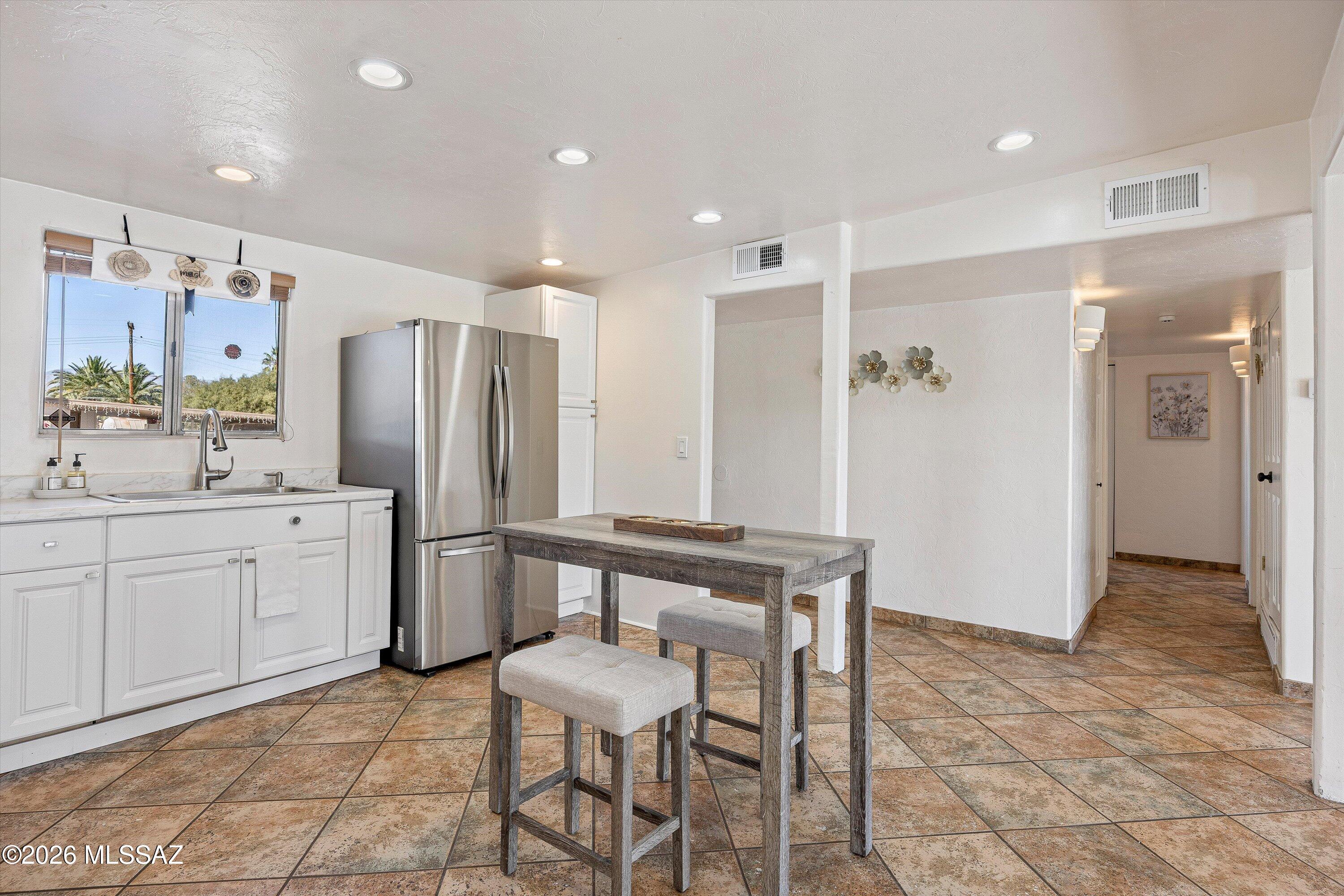 Kitchen with white cabinets, stainless steel refrigerator, and rustic gray dining table on terracotta tile.