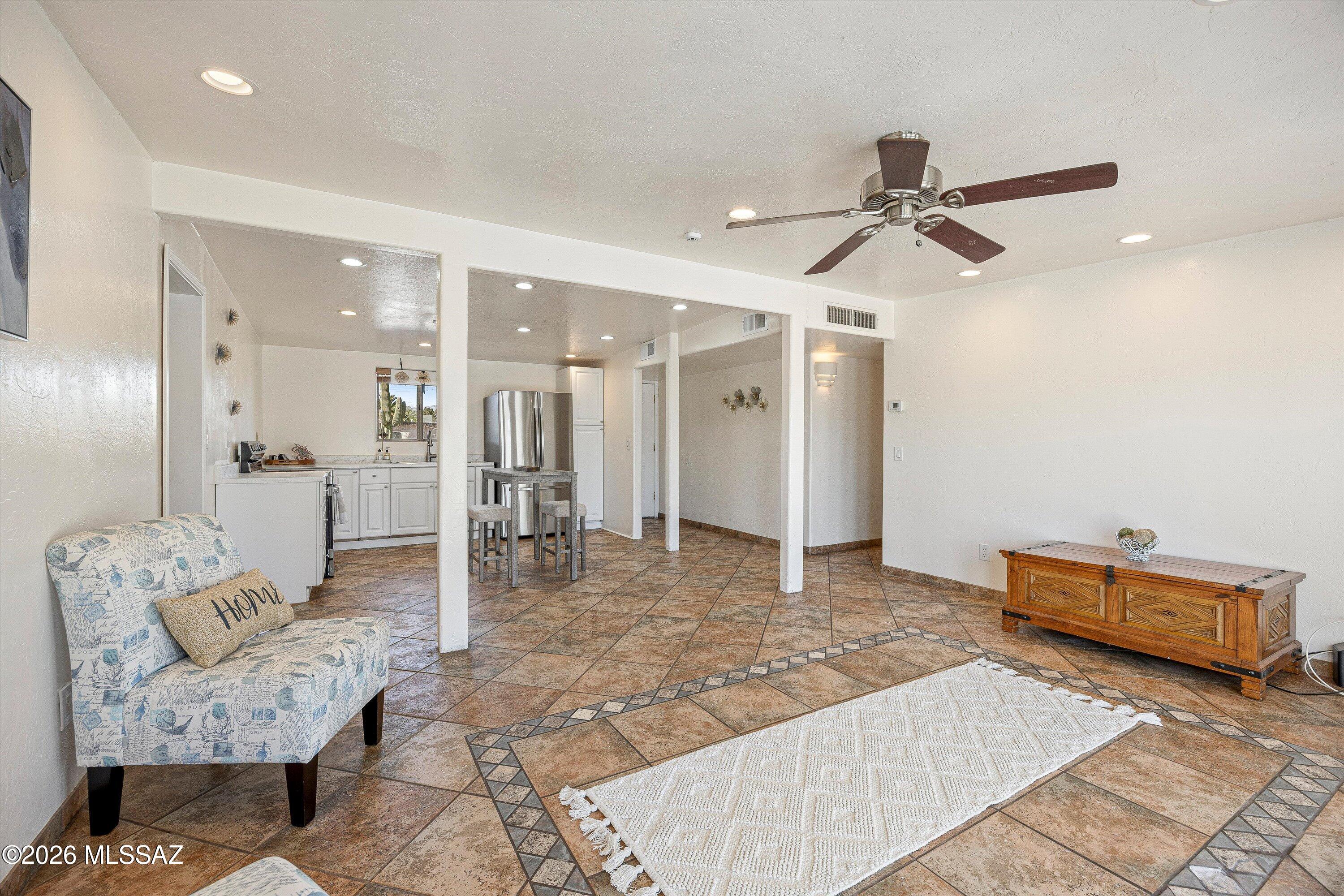 Open-plan living area with patterned tile floors, a ceiling fan, and a kitchen with stainless-steel appliances.