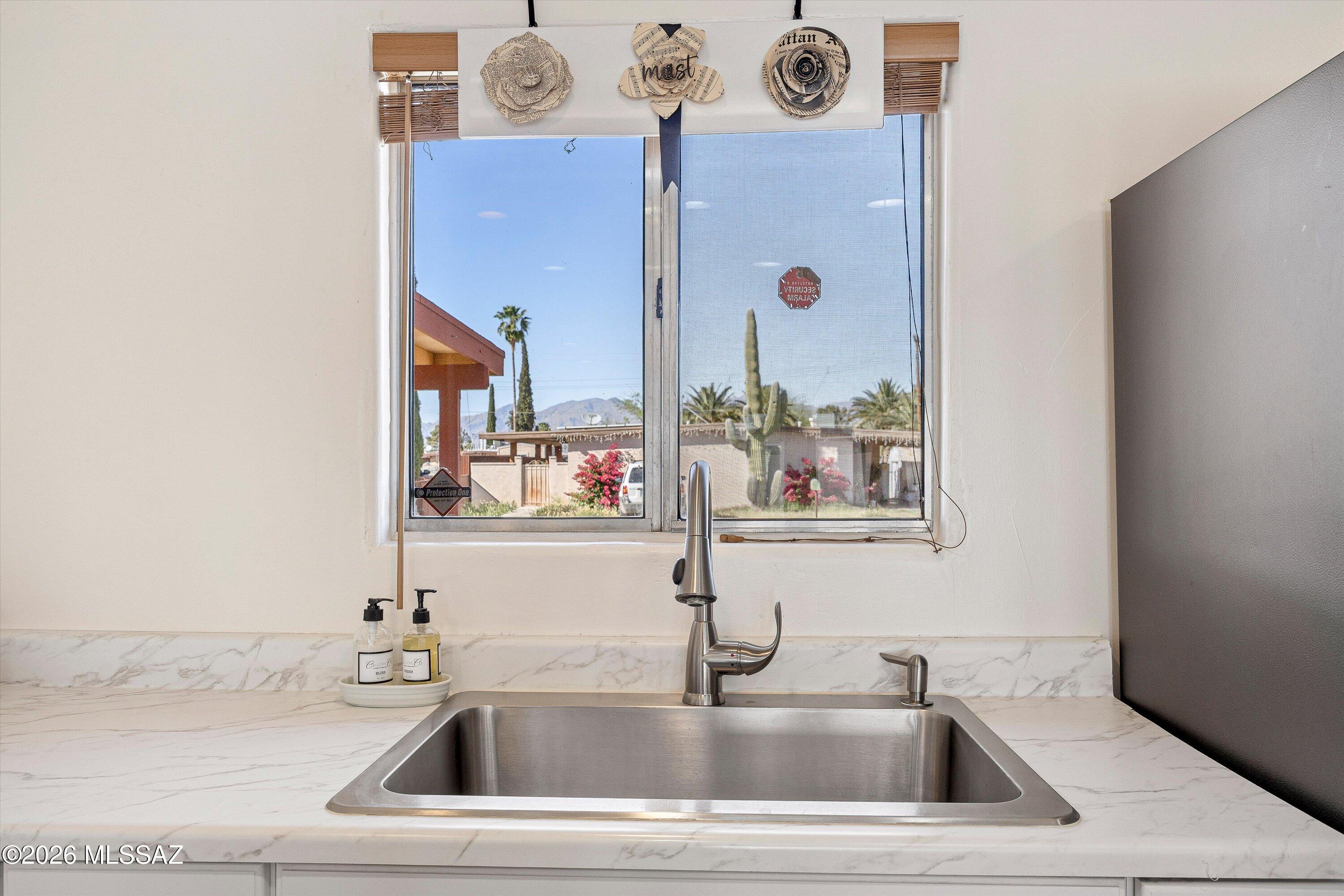 Kitchen sink with a tall stainless faucet, marble-look counters, and a window view of cacti and mountains.
