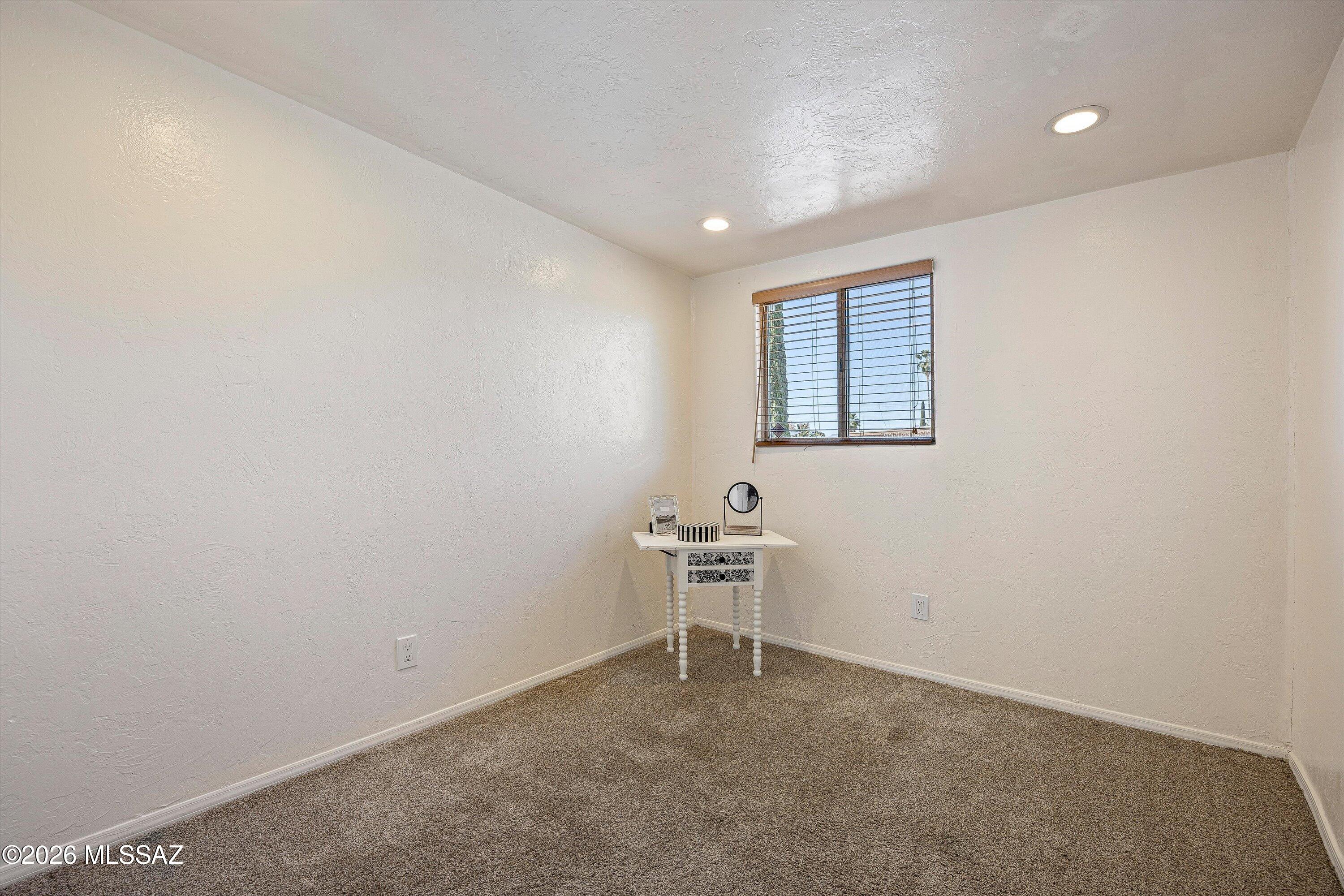Carpeted room with a small table beneath a window with blinds.