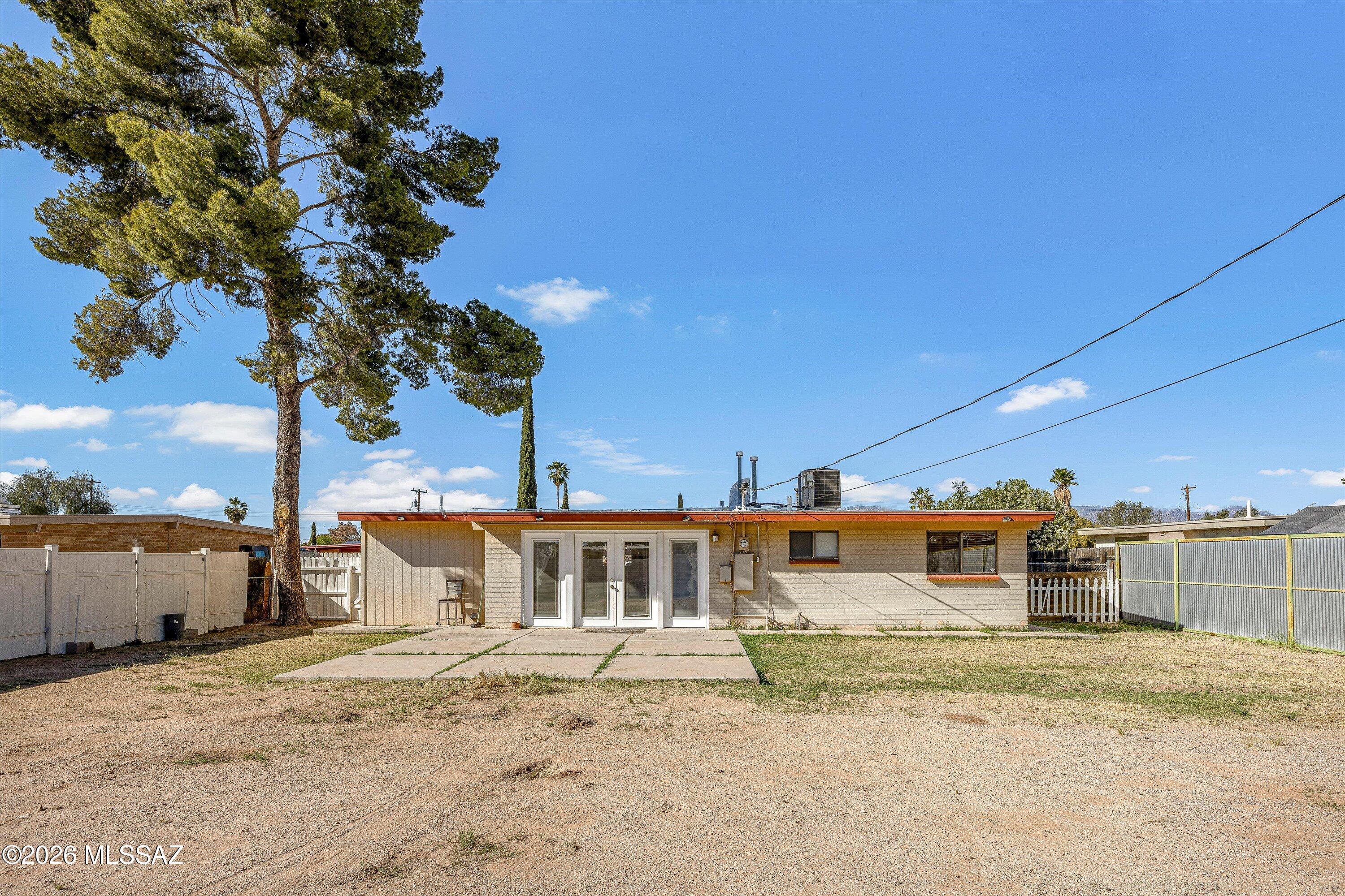 Rear of a single-story house with orange roof trim, sliding glass doors, and a dry fenced yard.