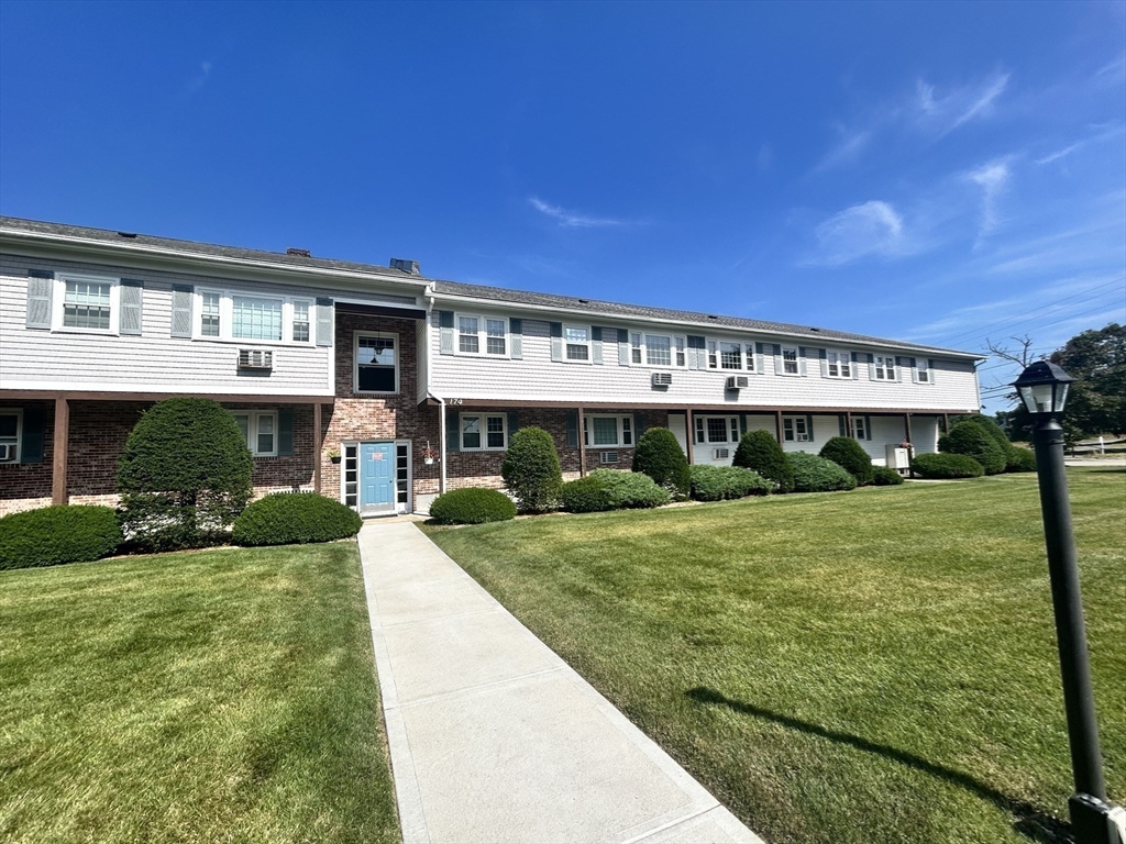 Two-story residential building with white siding, brick accents, blue entrance door, and landscaped lawn.