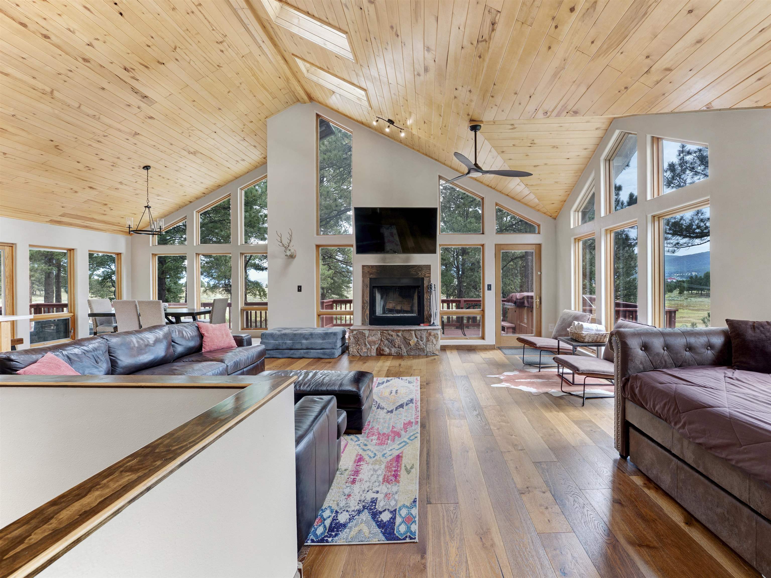 Vaulted living room with a stone fireplace, large windows, leather sofas, and mountain views.