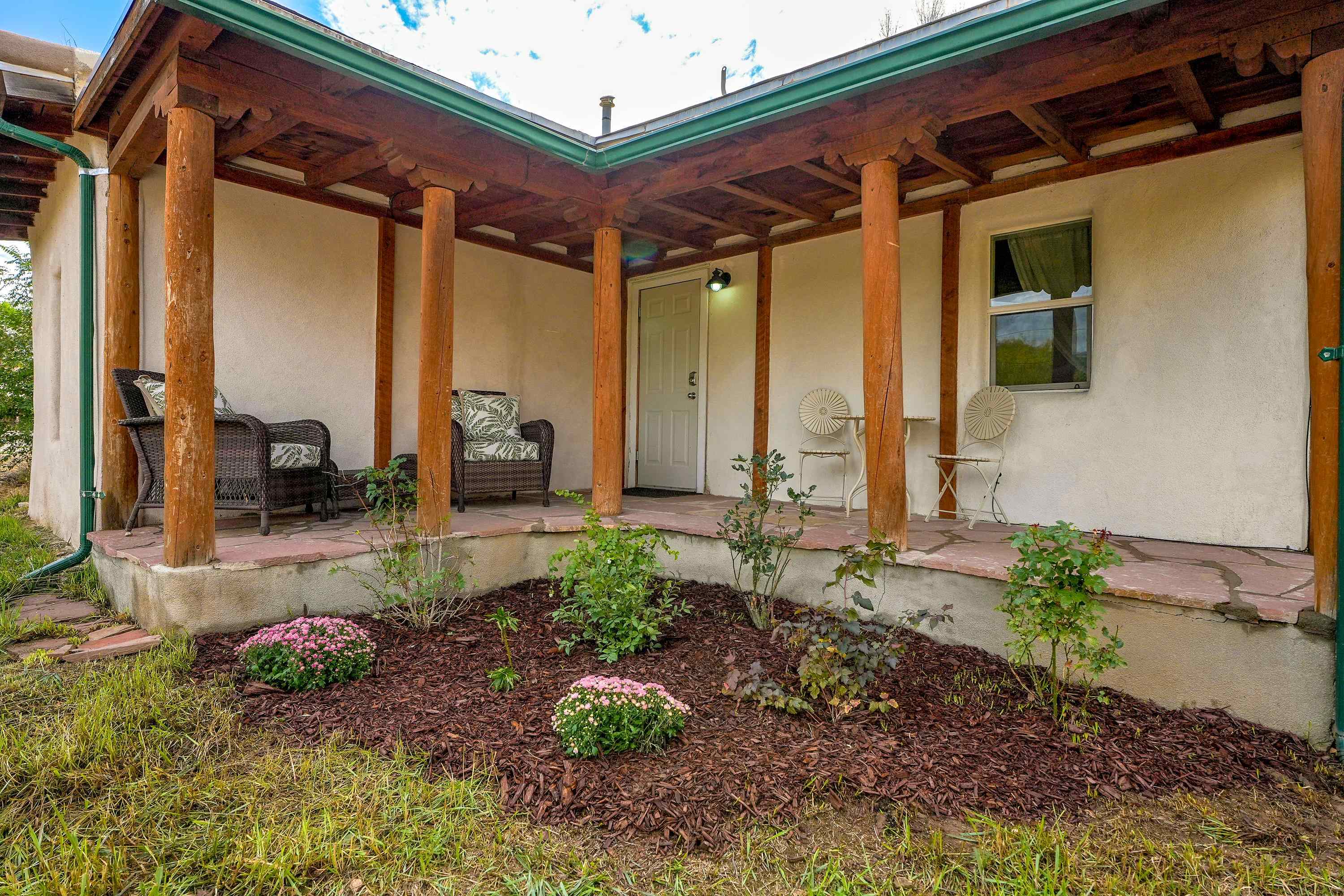 Covered front porch with timber posts, wicker seating, and flowering shrubs along the entry.