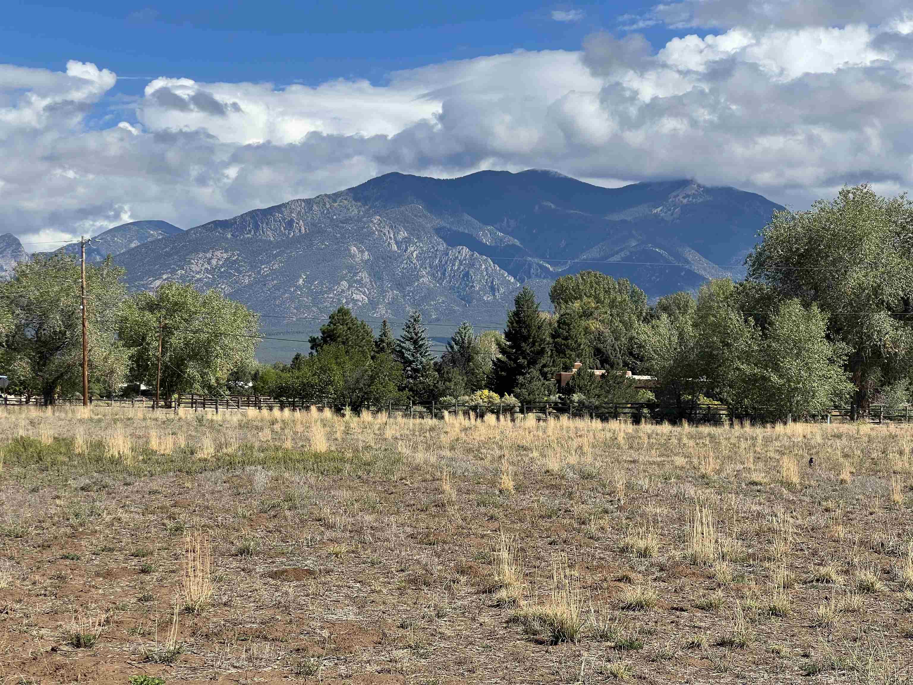 Open field with mountain views, trees, and fencing in the Taos area.