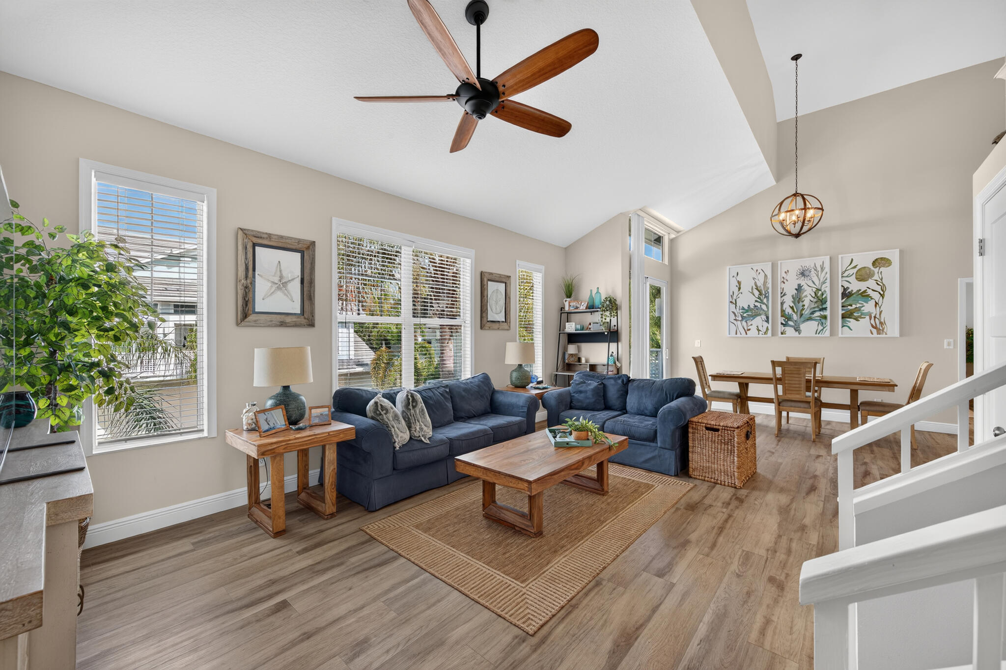 Open-plan living and dining room with blue sofas, large windows, and a wood dining table.