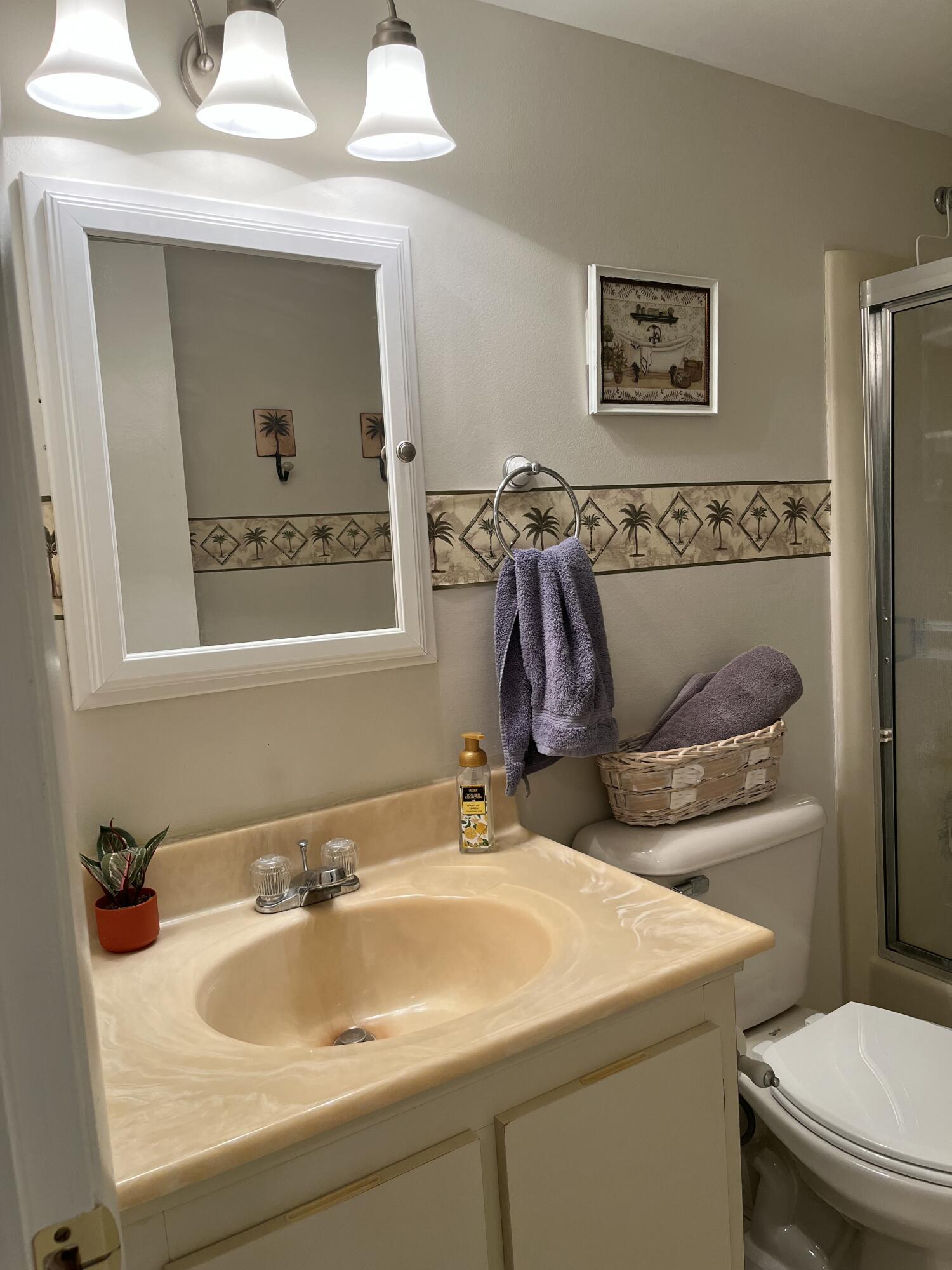 Bathroom with beige vanity, palm-tree wall border, purple towels, and glass shower.