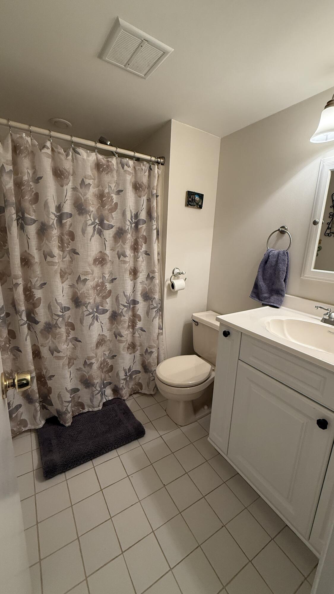 Bathroom with a floral shower curtain, white vanity, toilet, and tiled floor.
