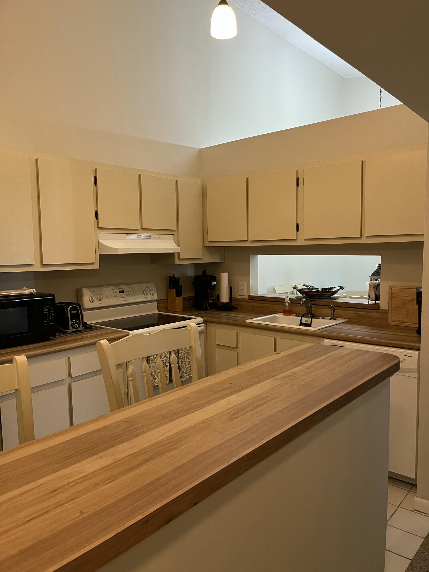 Kitchen with cream cabinets, white electric range, and long wooden breakfast bar.