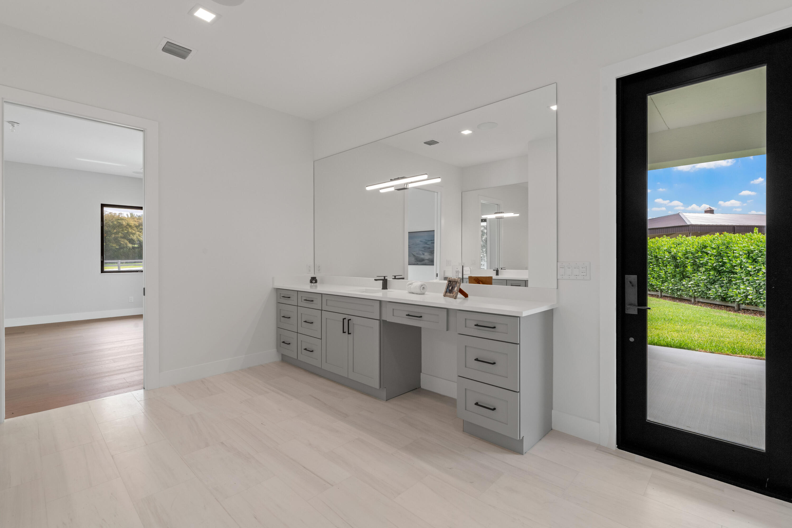 Modern bathroom vanity with gray cabinetry, a large mirror, and a glass door to the patio.
