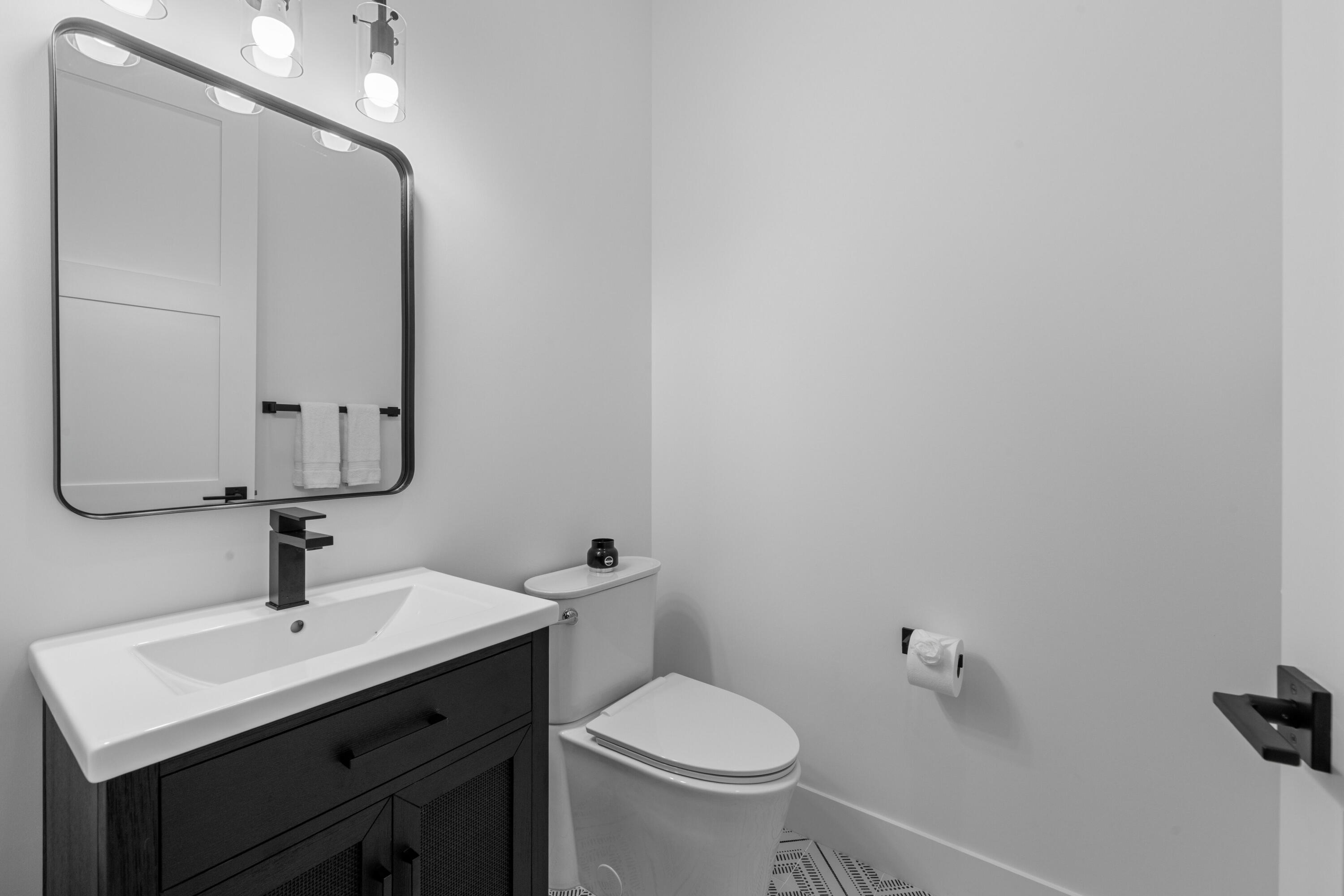 Modern bathroom with a dark wood vanity, black faucet, and large framed mirror beside the toilet.