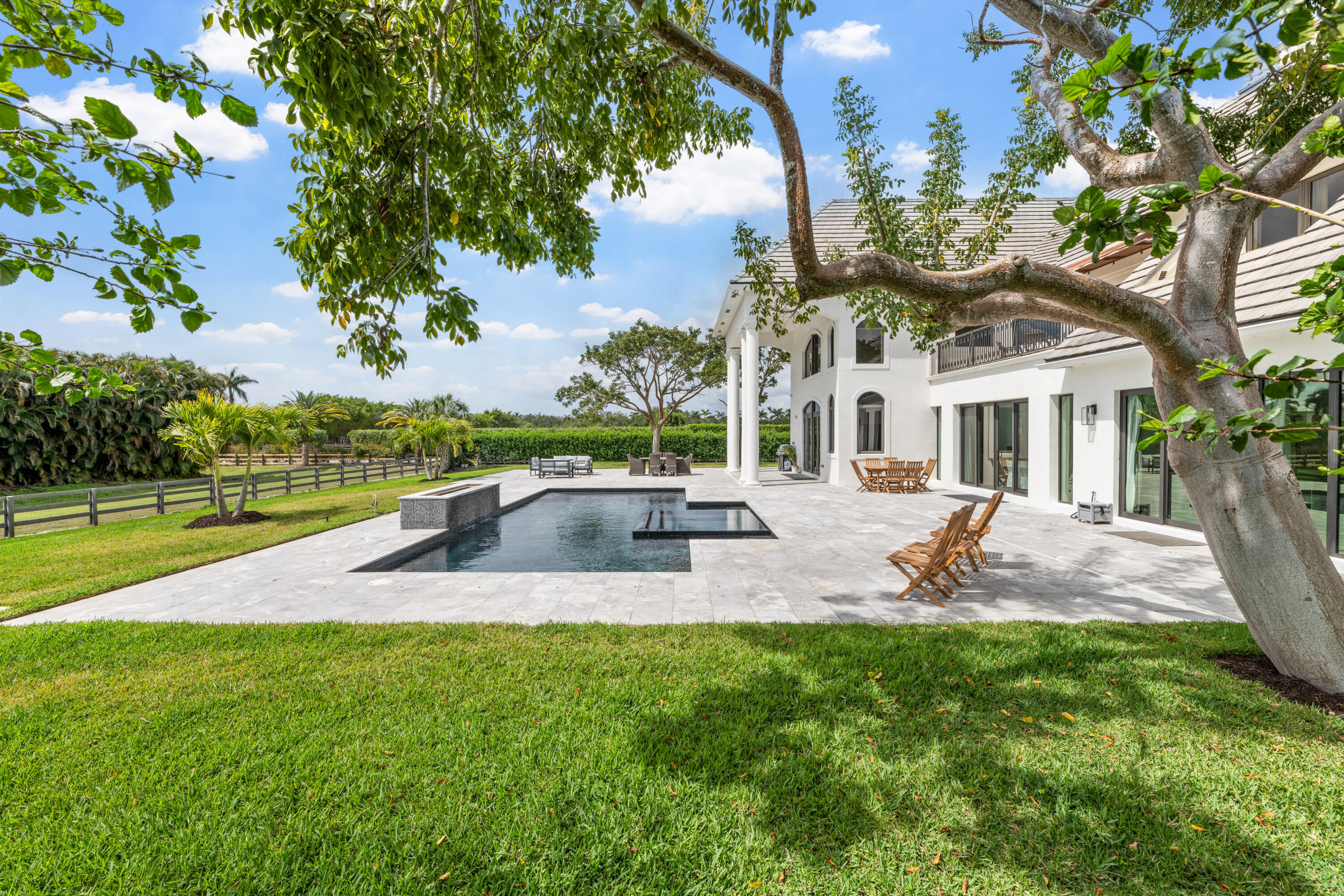 White two-story home beside a stone patio and rectangular pool, framed by mature trees.