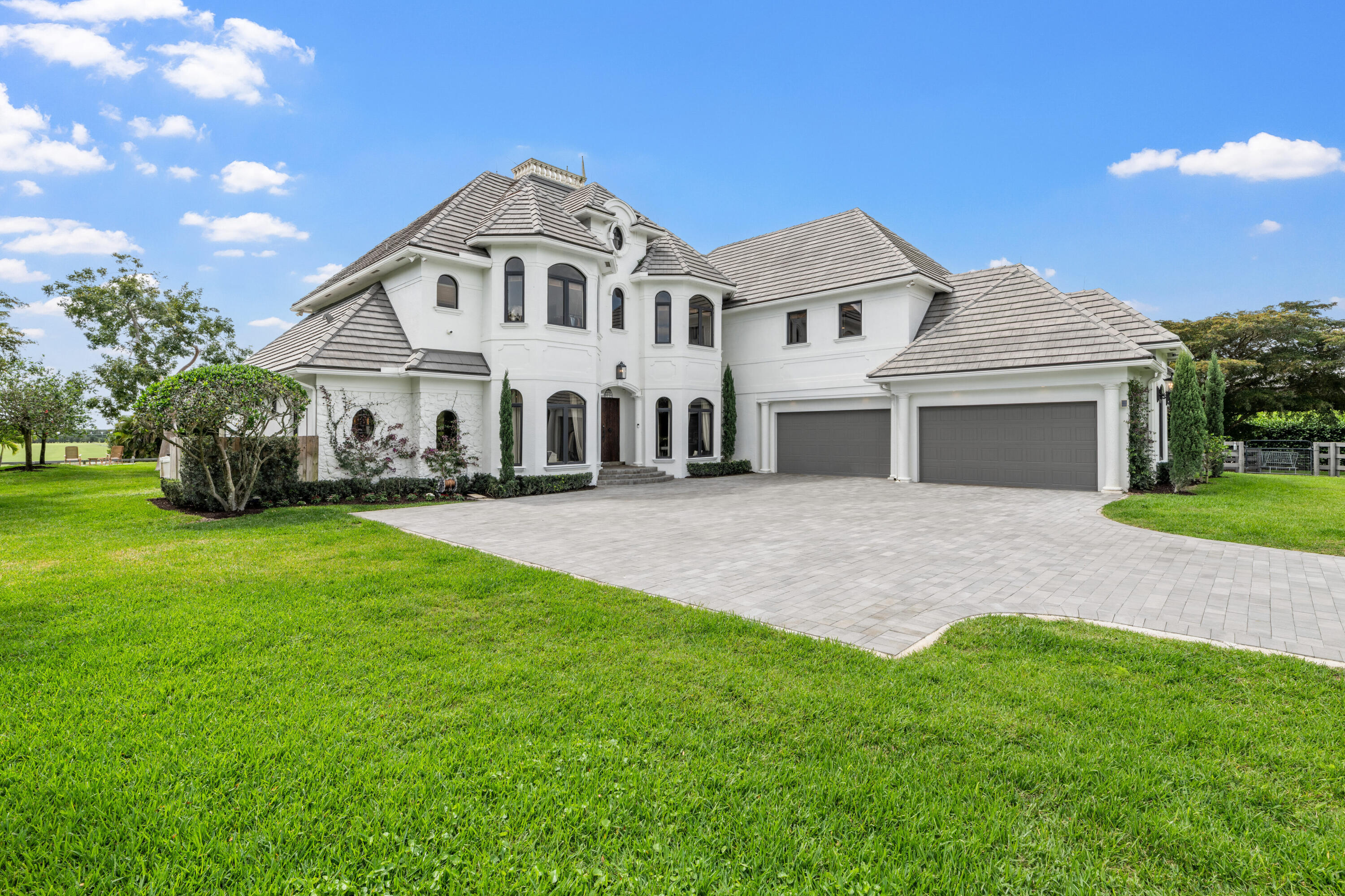 Two-story white stucco home with gray tile roofs, a three-car garage, and a wide paved driveway.