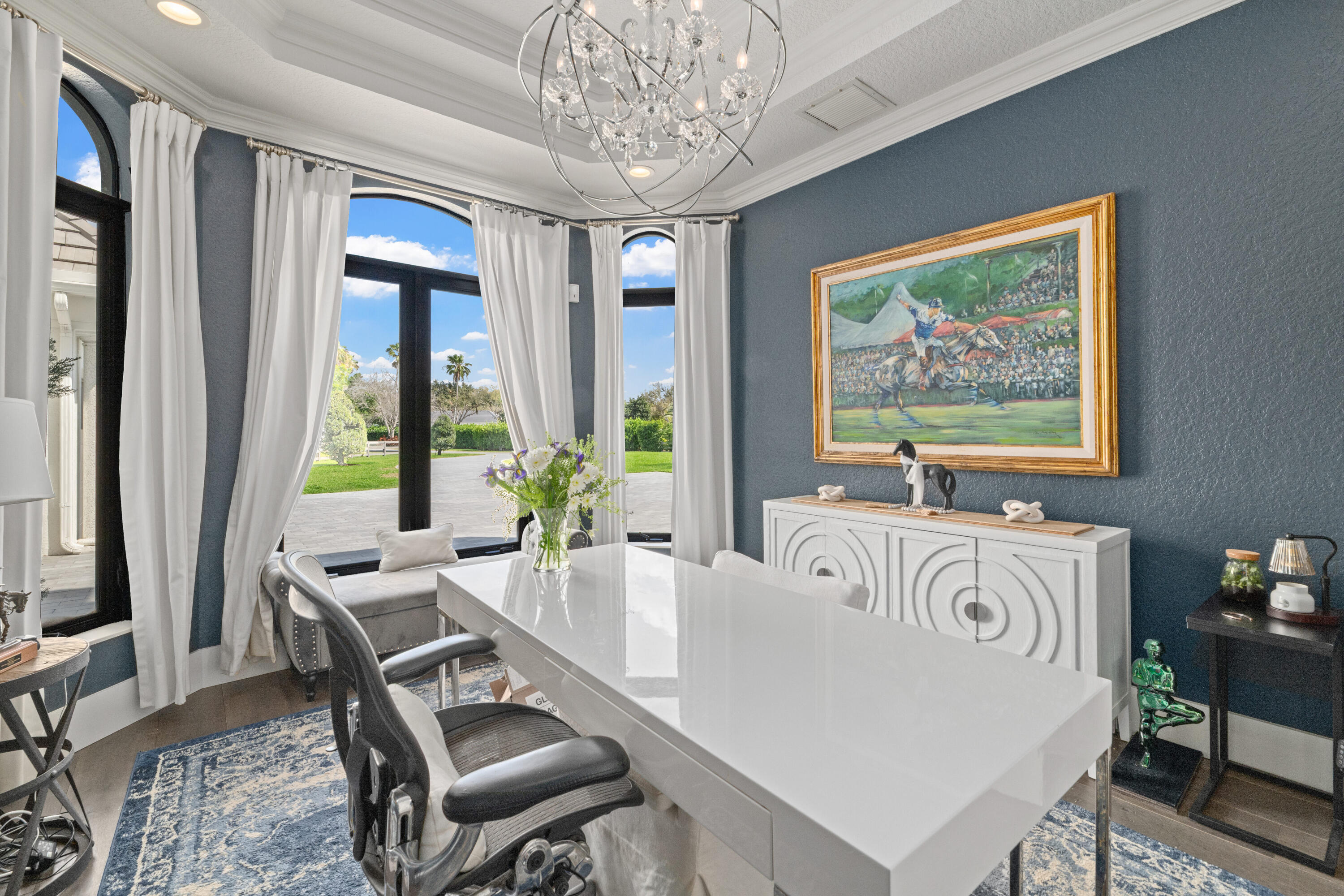 Dining room with a glossy white table, arched windows, and views of a green lawn.