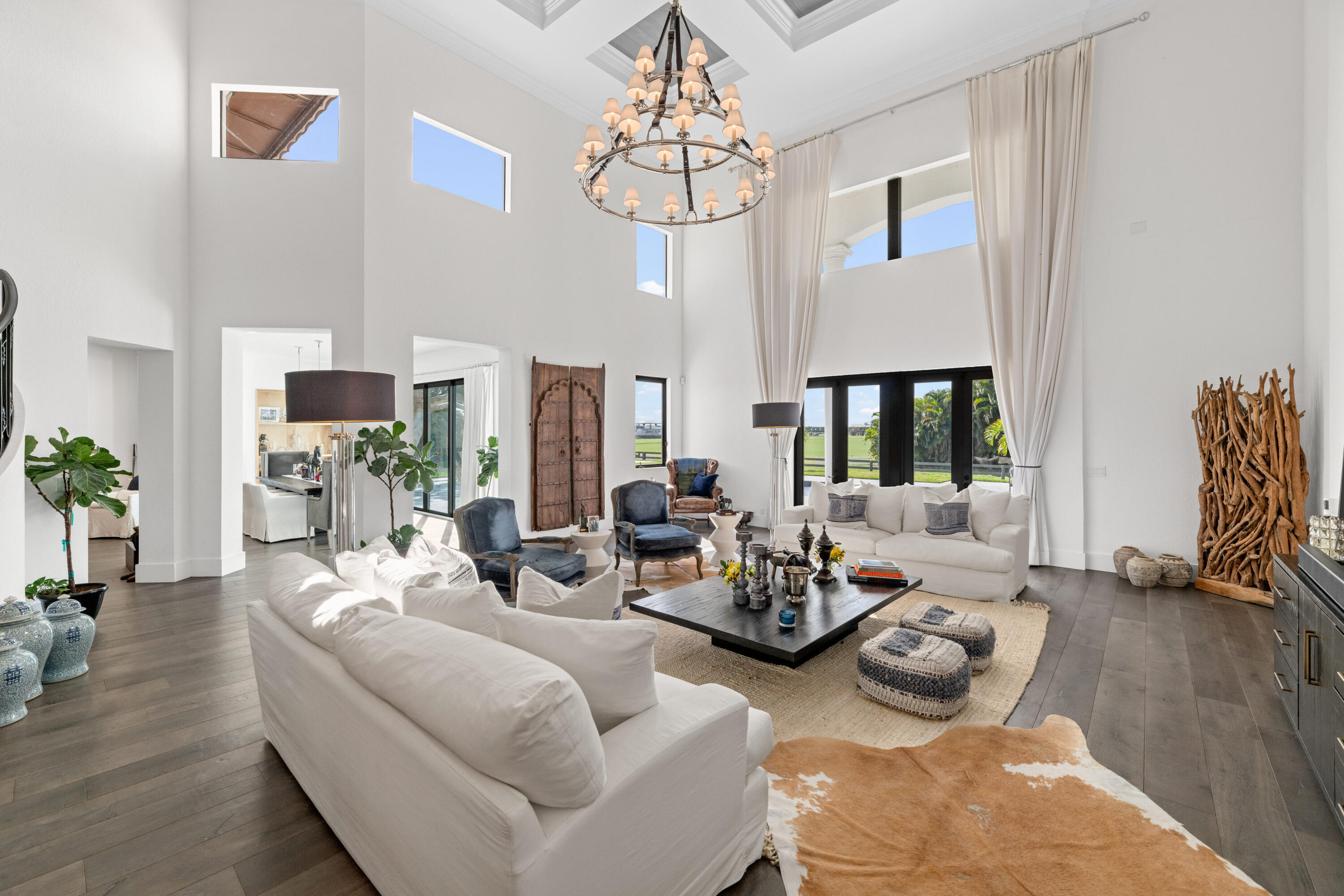 Double-height living room with white sofas, tall windows, and a circular chandelier.