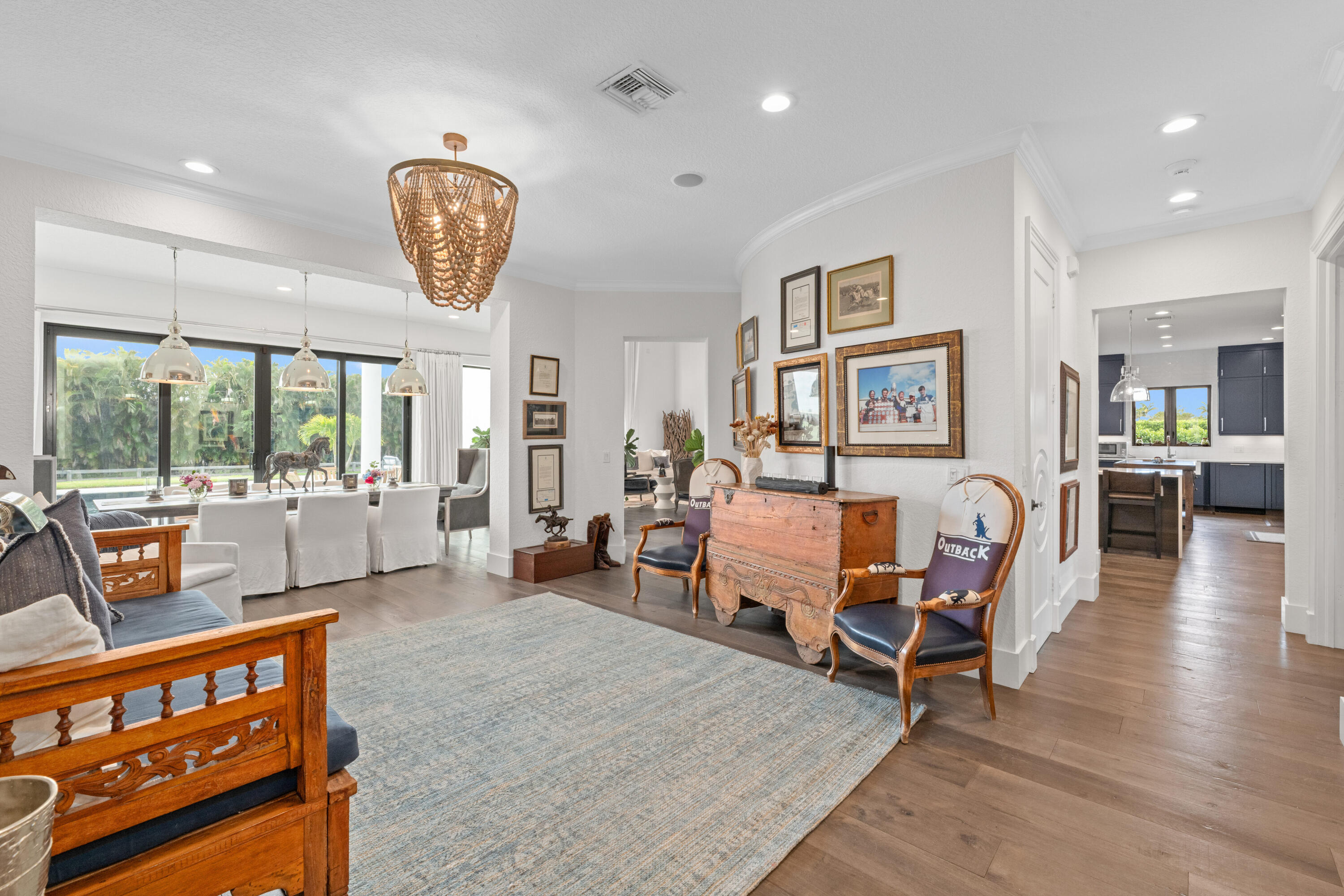 Open-plan living room with carved wood furnishings, framed pictures, and a dining area by large garden-facing windows.