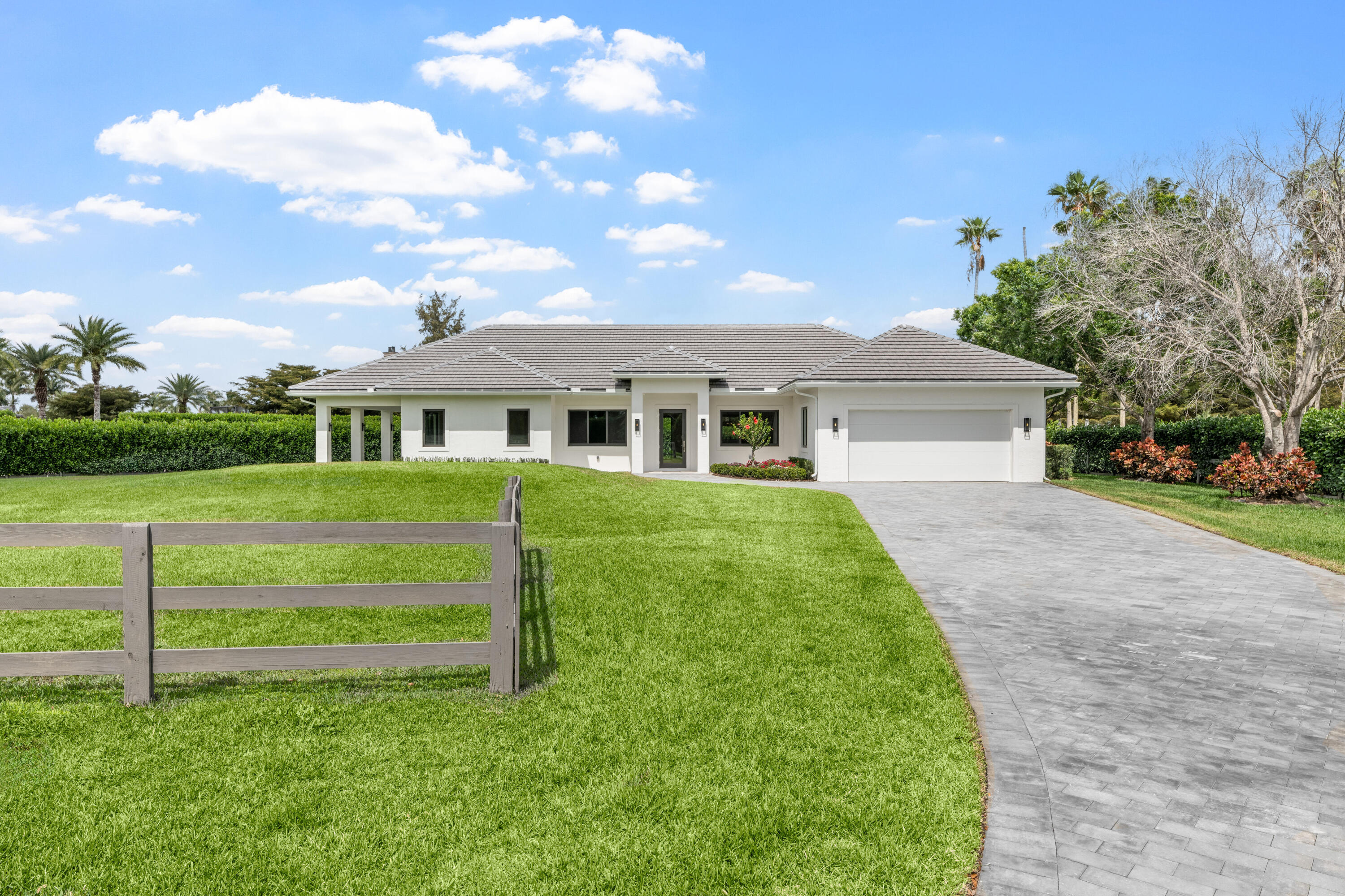 Single-story white home with a gray tiled roof, broad lawn, and curved paver driveway.