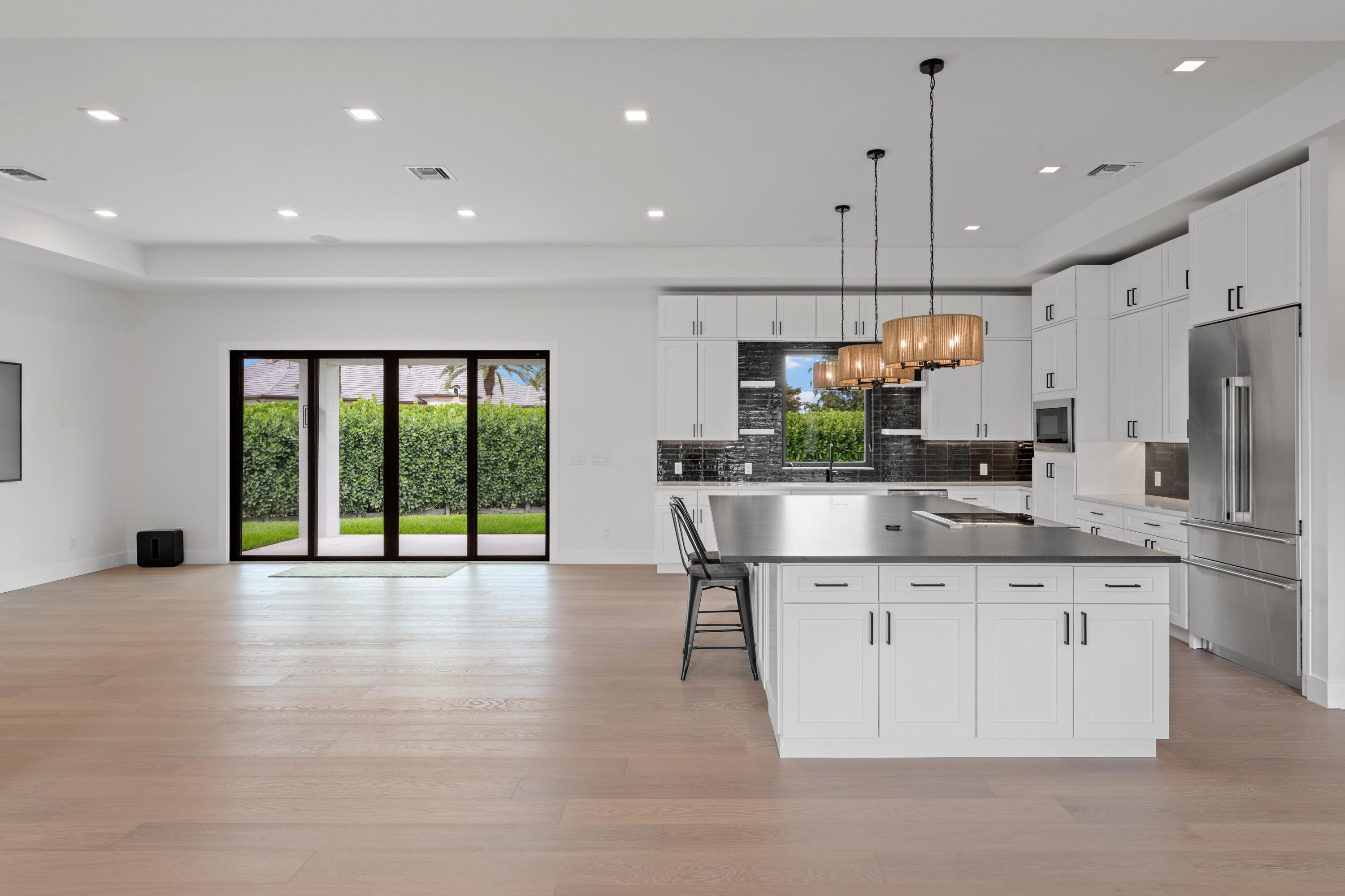 Open kitchen with a large stainless-steel island, white cabinets, and sliding doors to the backyard.