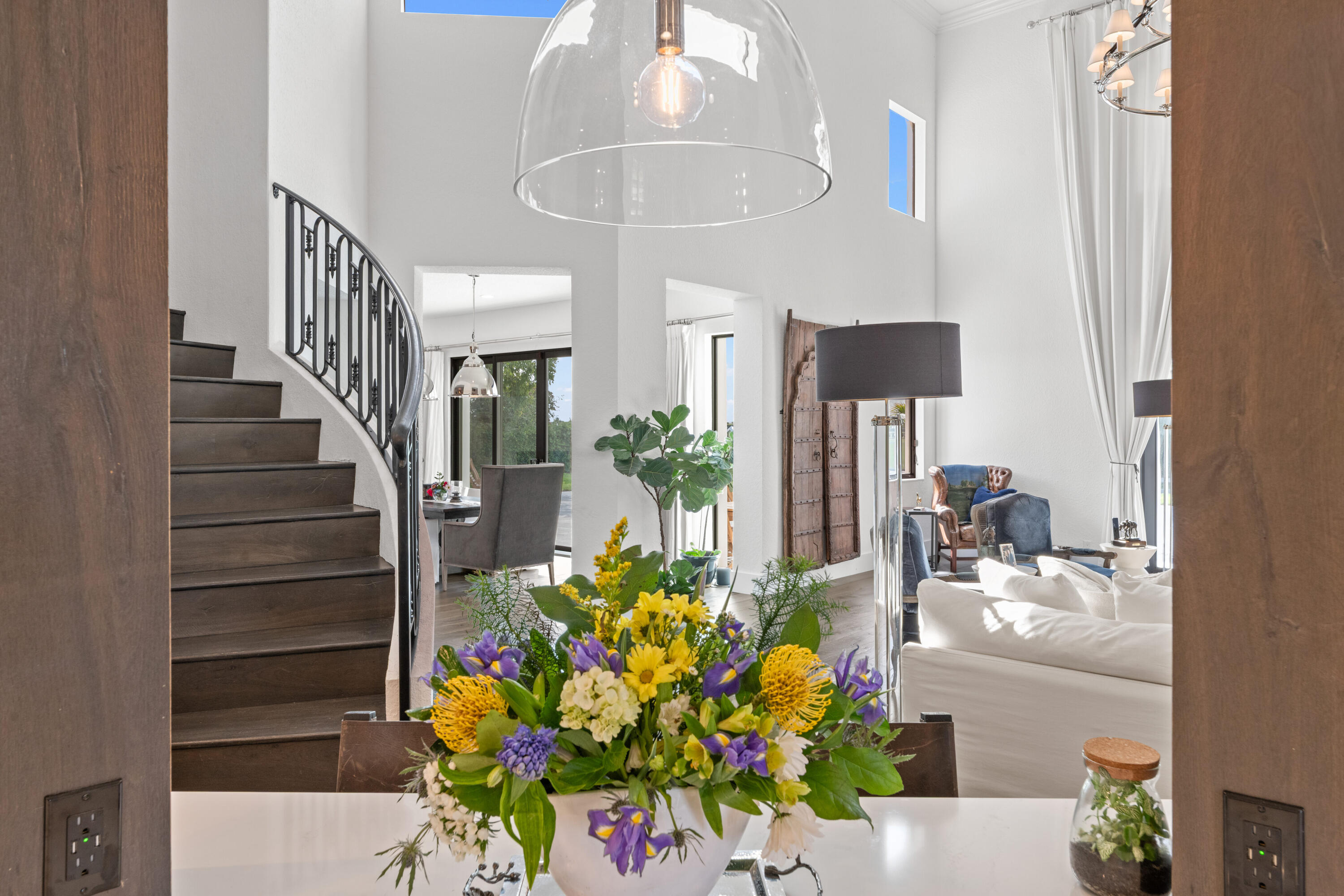 Bright home foyer with a curved staircase, tall ceilings, and a colorful floral arrangement in the foreground.