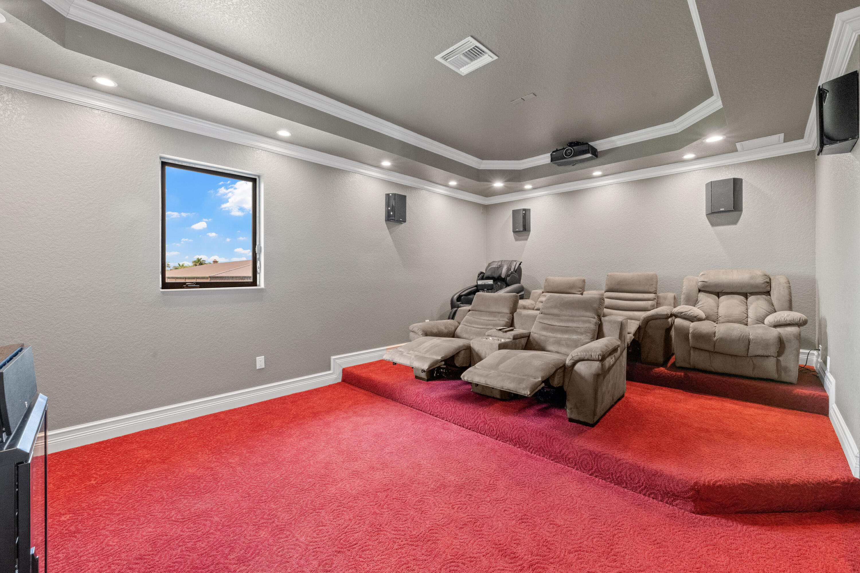 Home theater with tiered red carpet, reclining seats, and a ceiling-mounted projector.