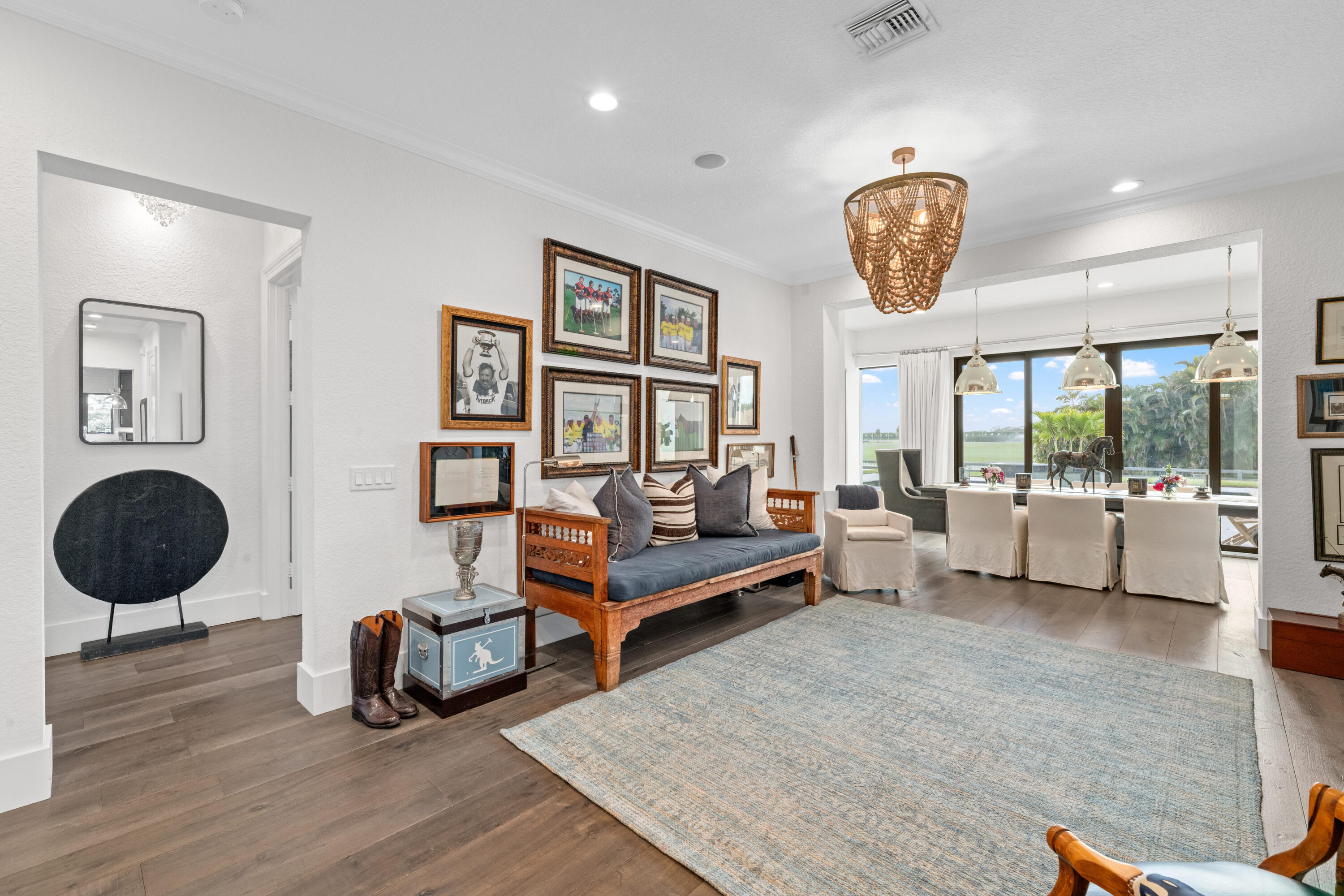 Living room with carved wooden sofa, framed sports photos, and dining area overlooking the lawn and water.