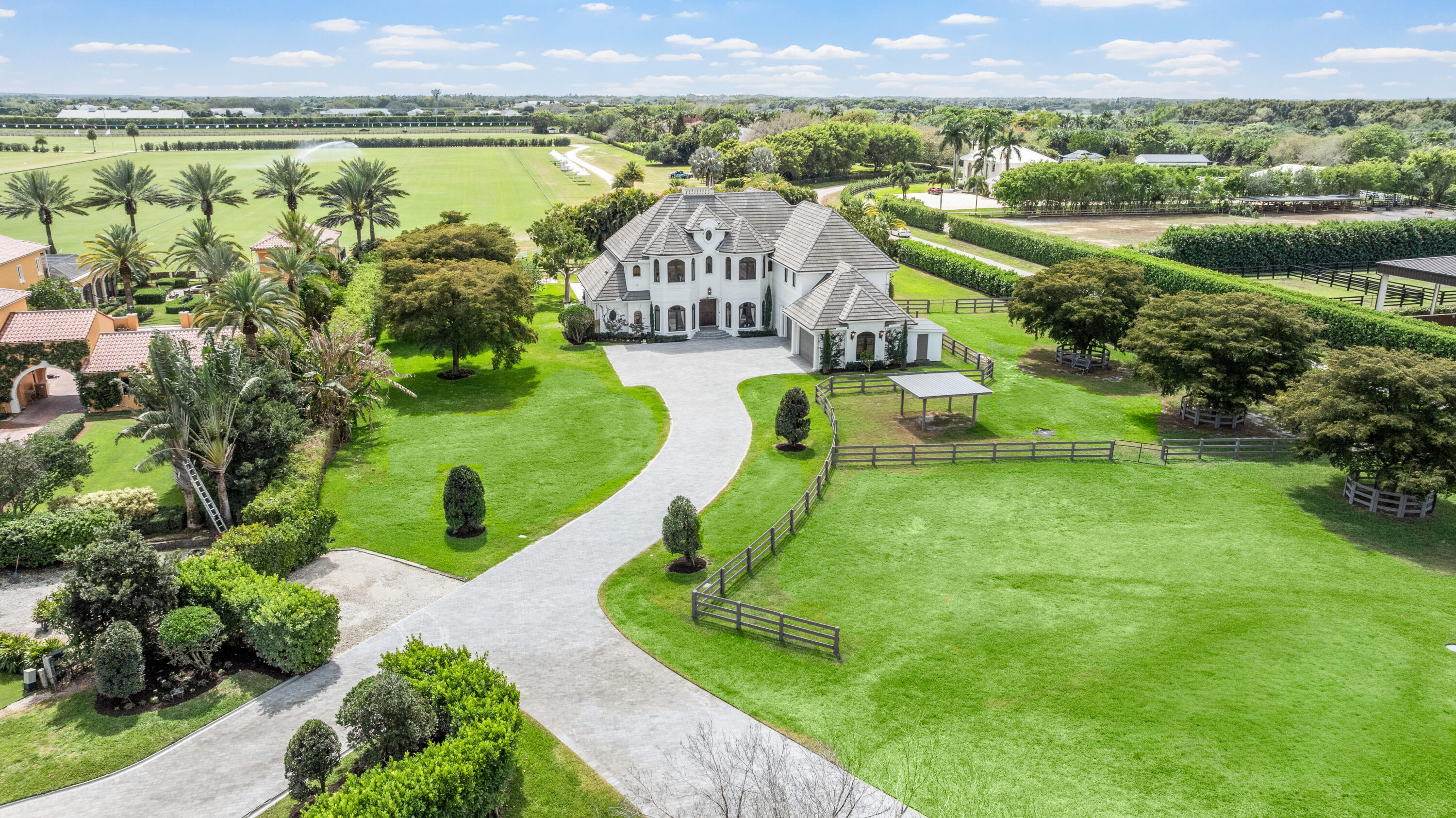 Aerial view of a white estate home with fenced paddocks and a polo field nearby.