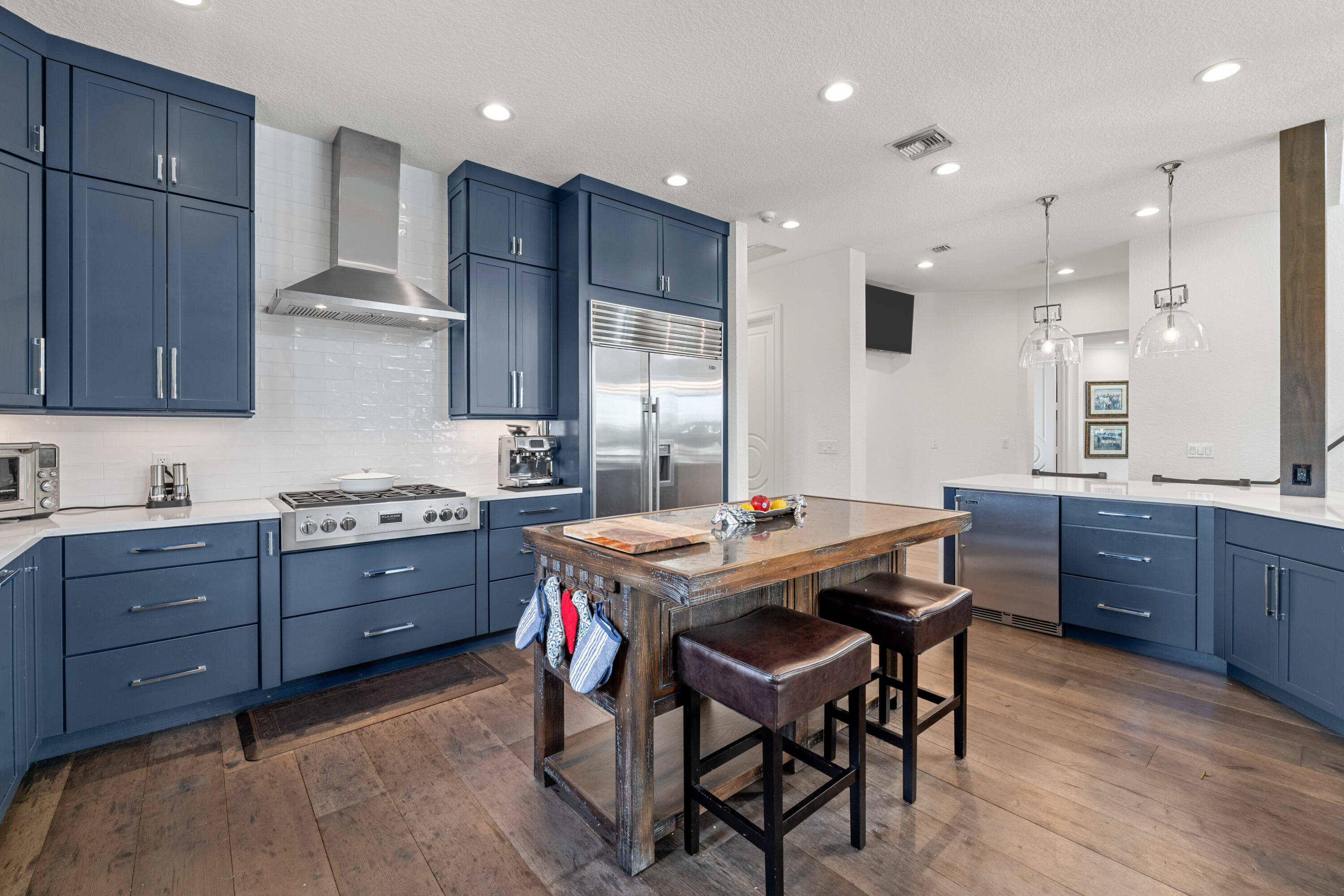 Kitchen with navy cabinets, stainless appliances, and a rustic wood island with leather stools.