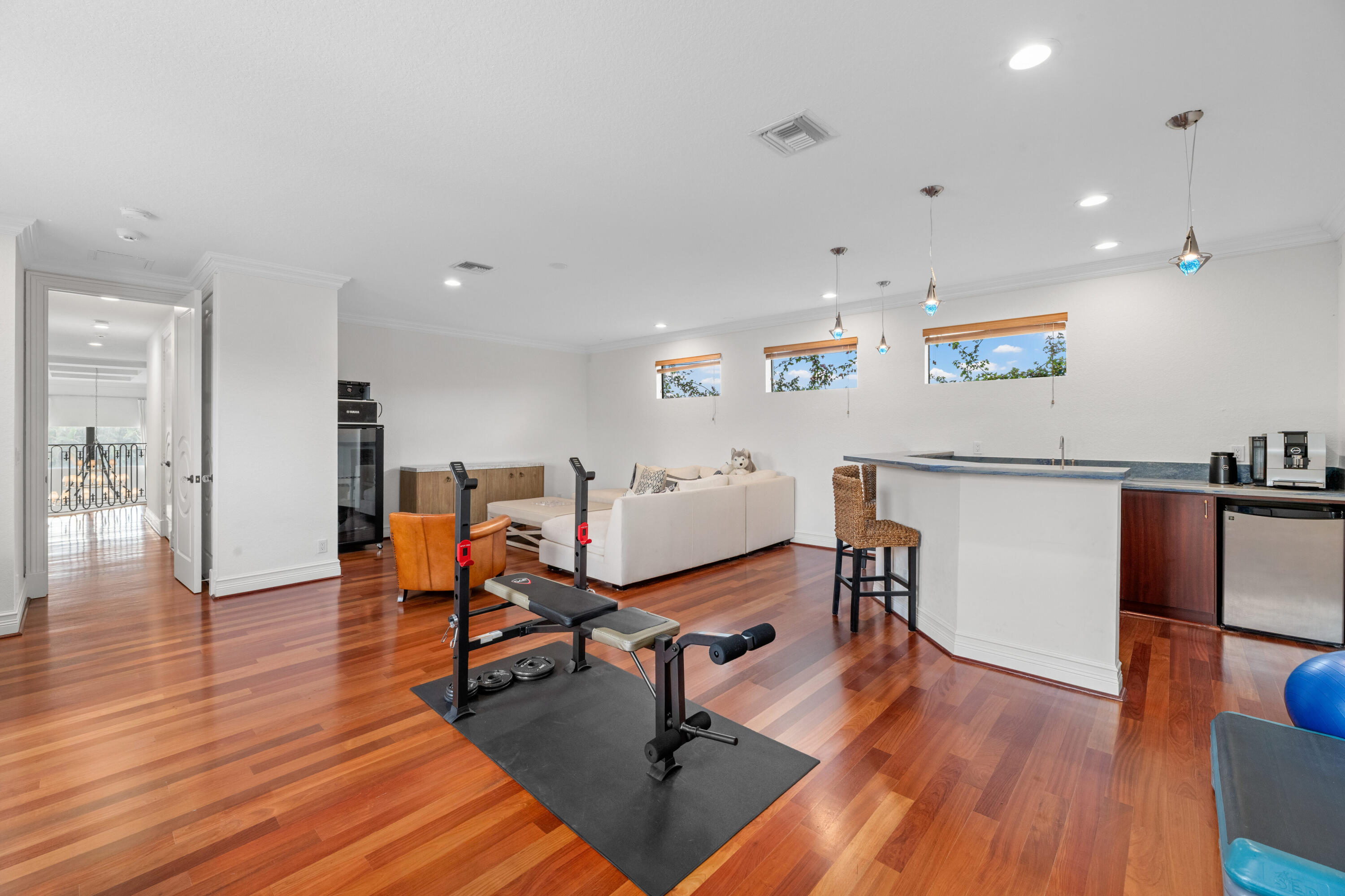 Multipurpose fitness room with exercise equipment, a white sofa, and a kitchenette with breakfast bar.
