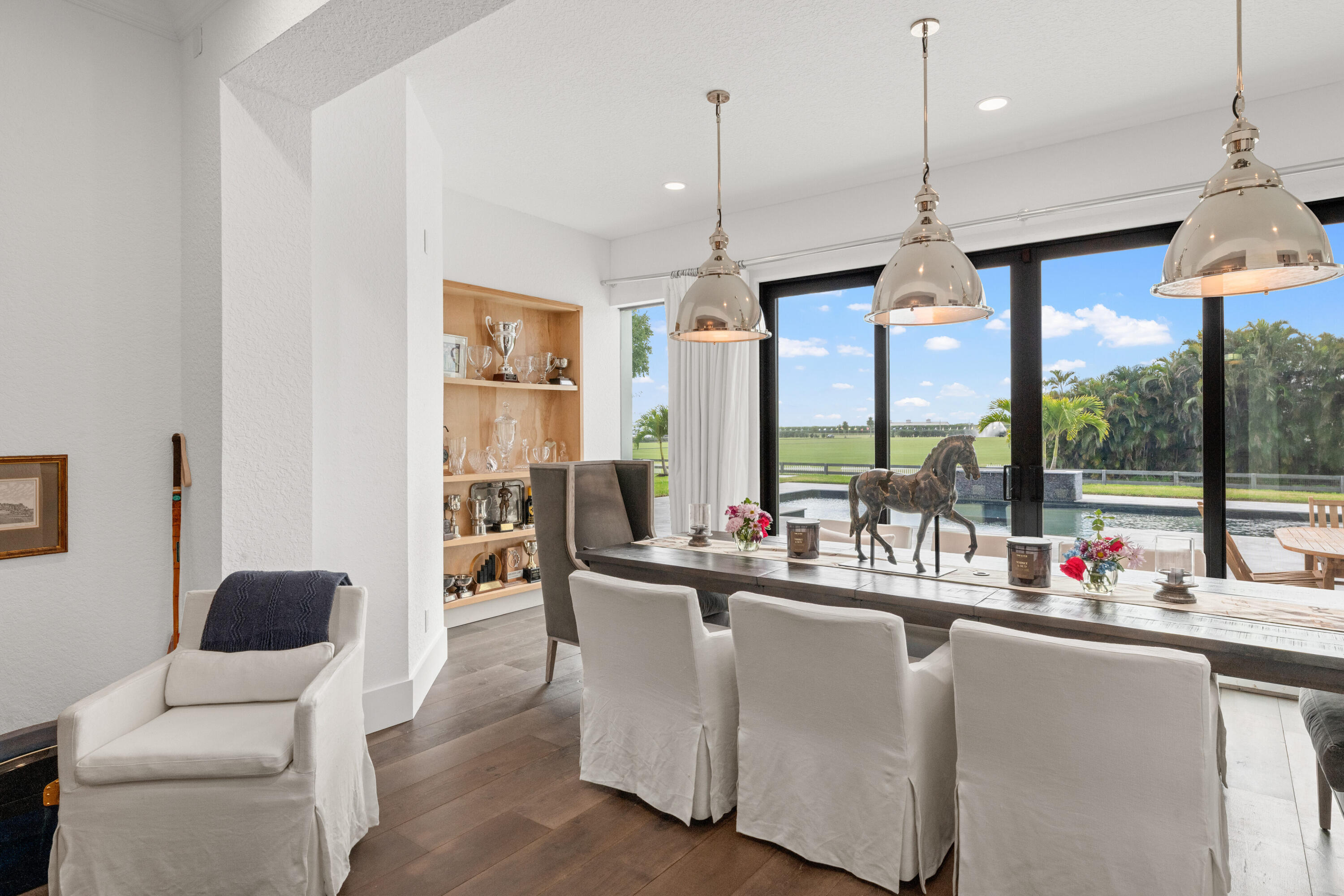Dining room with trophy shelves, pendant lights, and glass doors overlooking a pool terrace.