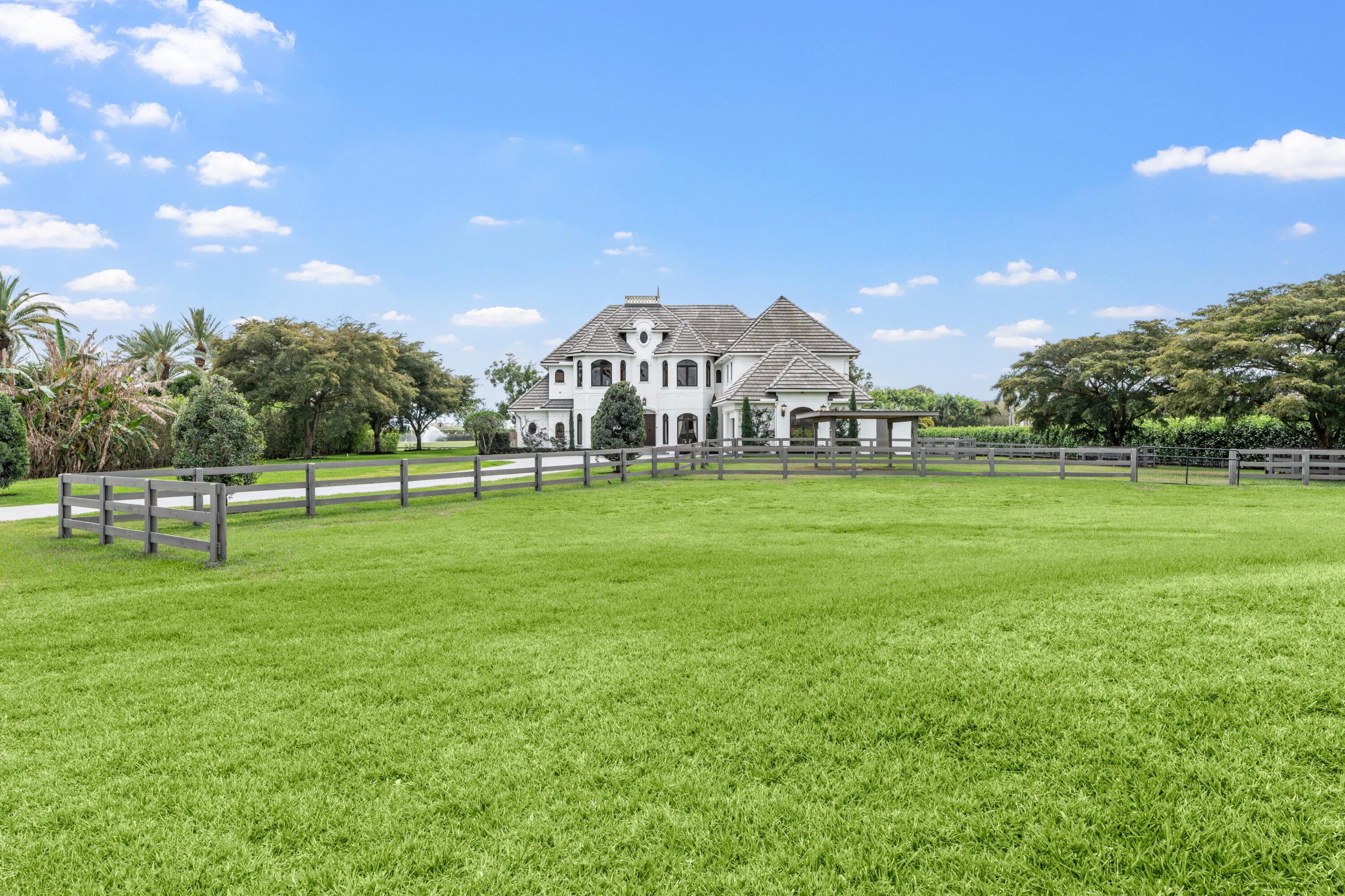Large white two-story home behind a rail fence, with an expansive green lawn and mature trees.