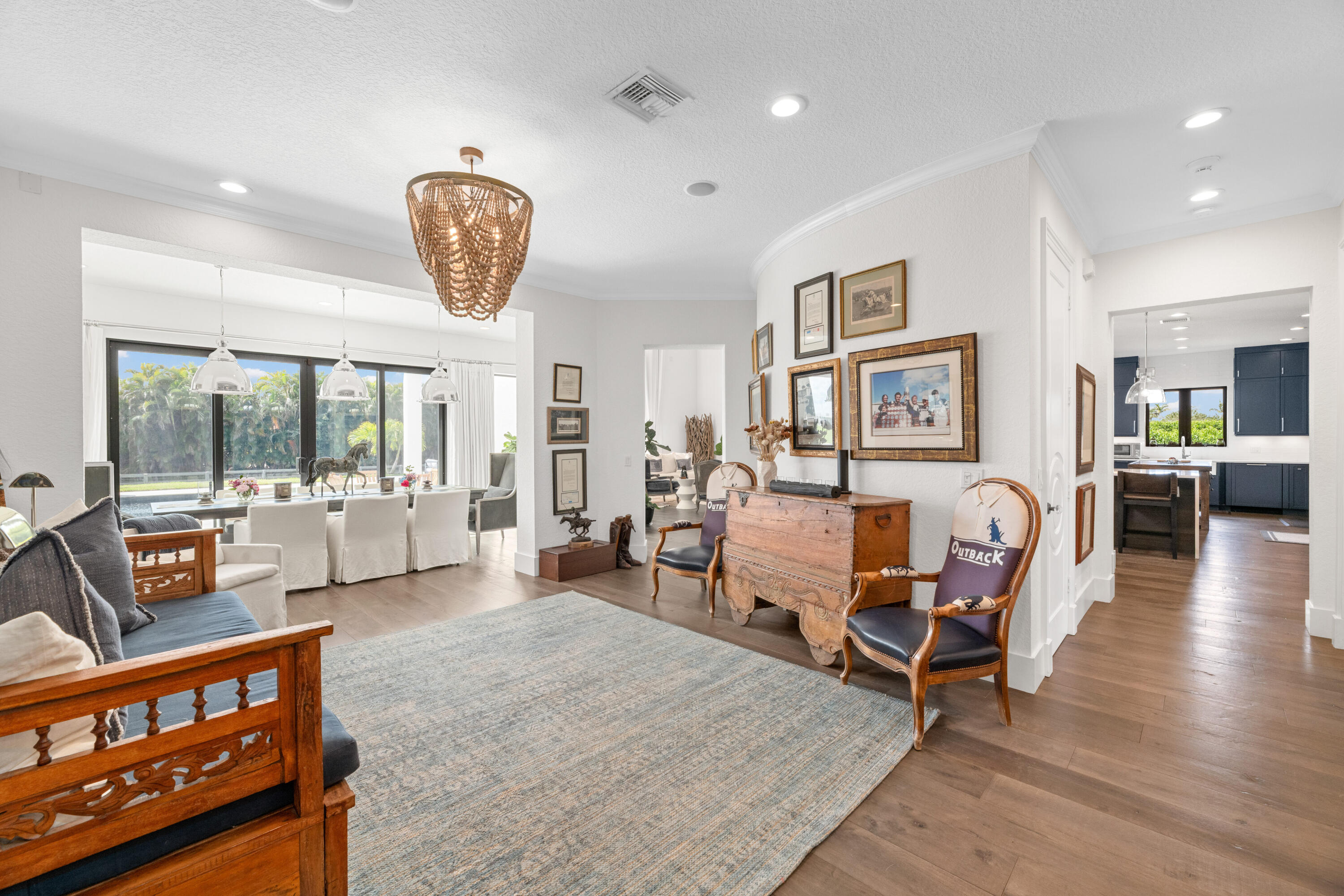 Furnished living and dining area with a woven chandelier, gallery wall, and windows overlooking tropical greenery.