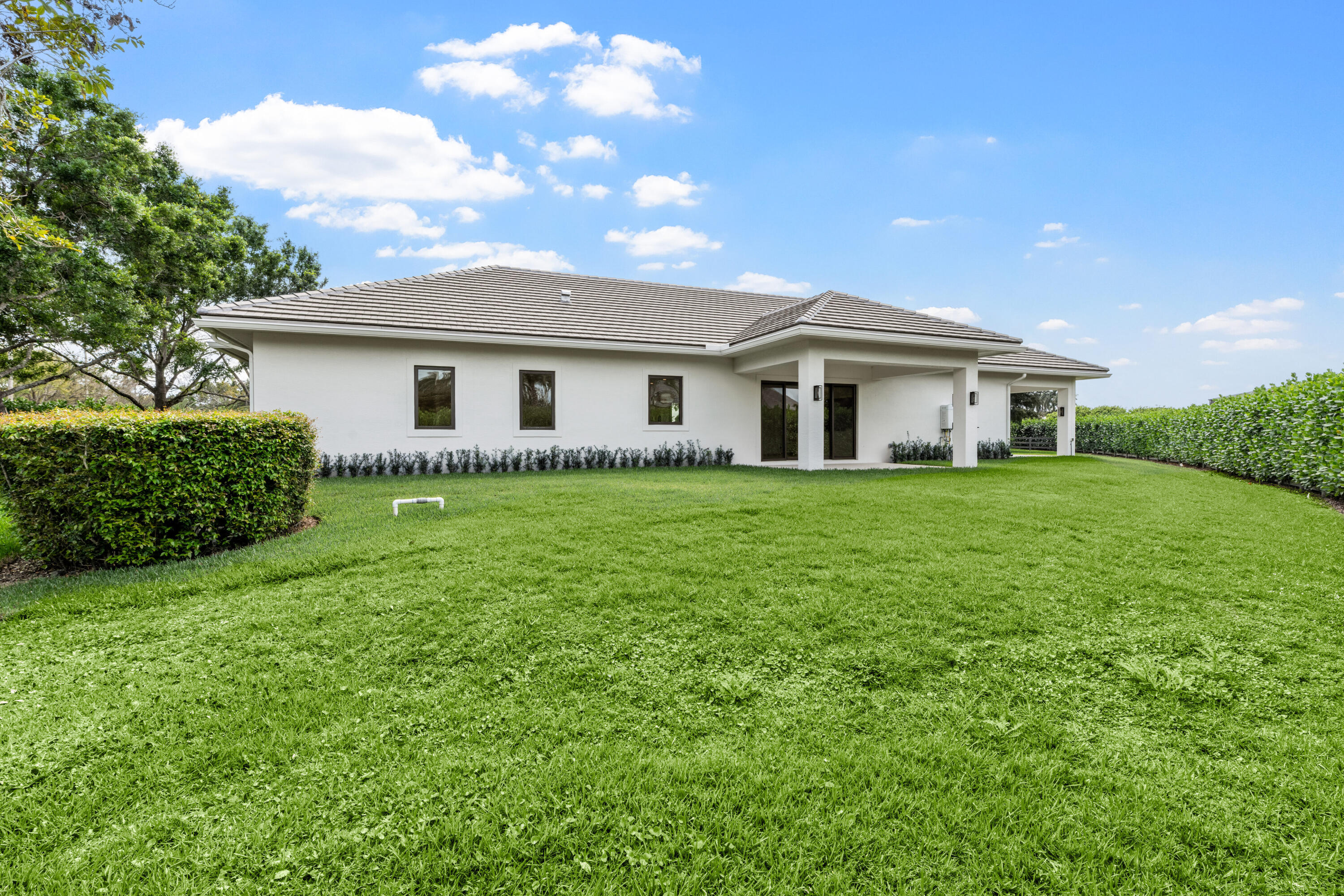 Rear of a white single-story home with a covered patio, broad lawn, and clipped hedges.