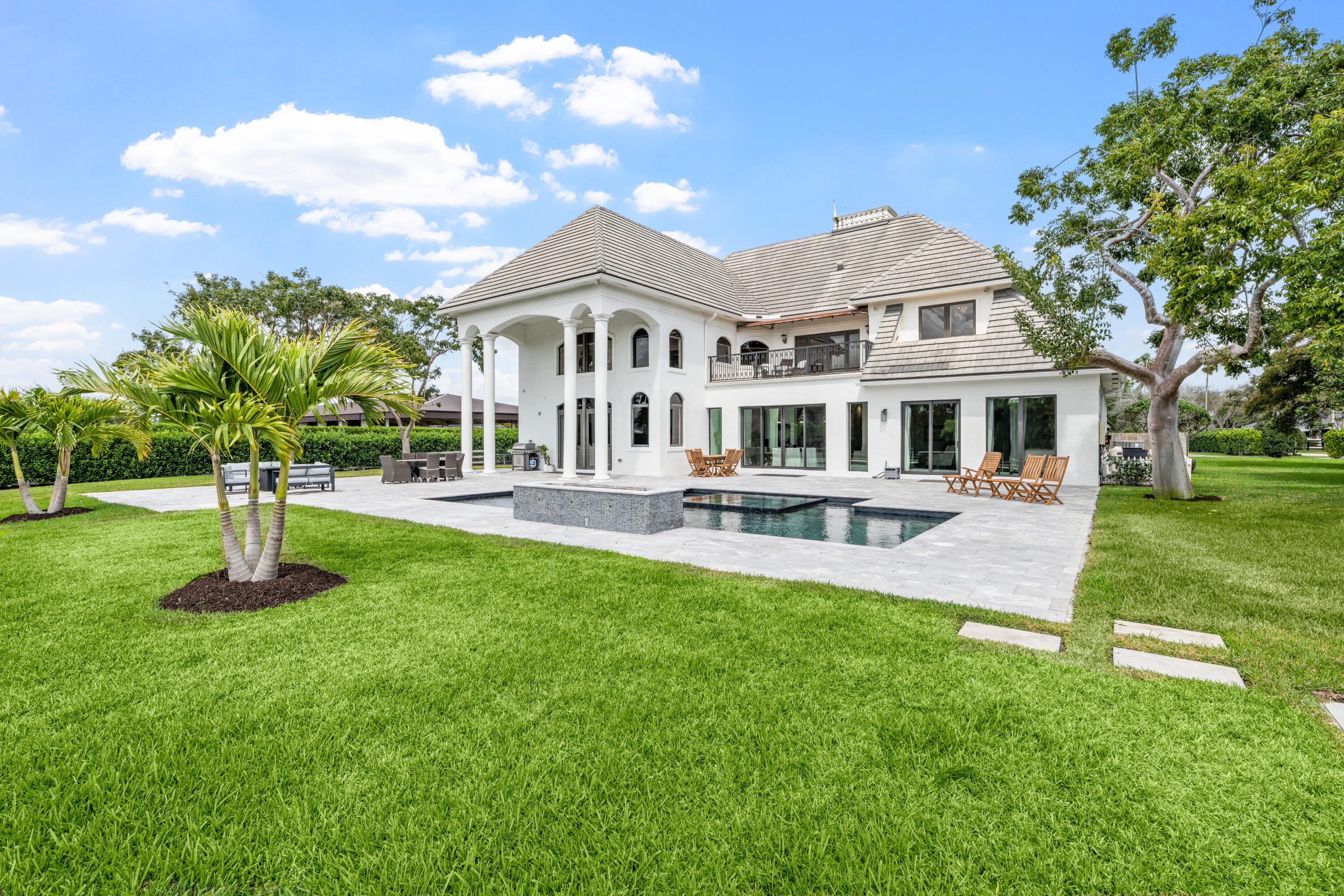 Rear of a white two-story home with an arched-column patio, swimming pool, and palm-lined lawn.