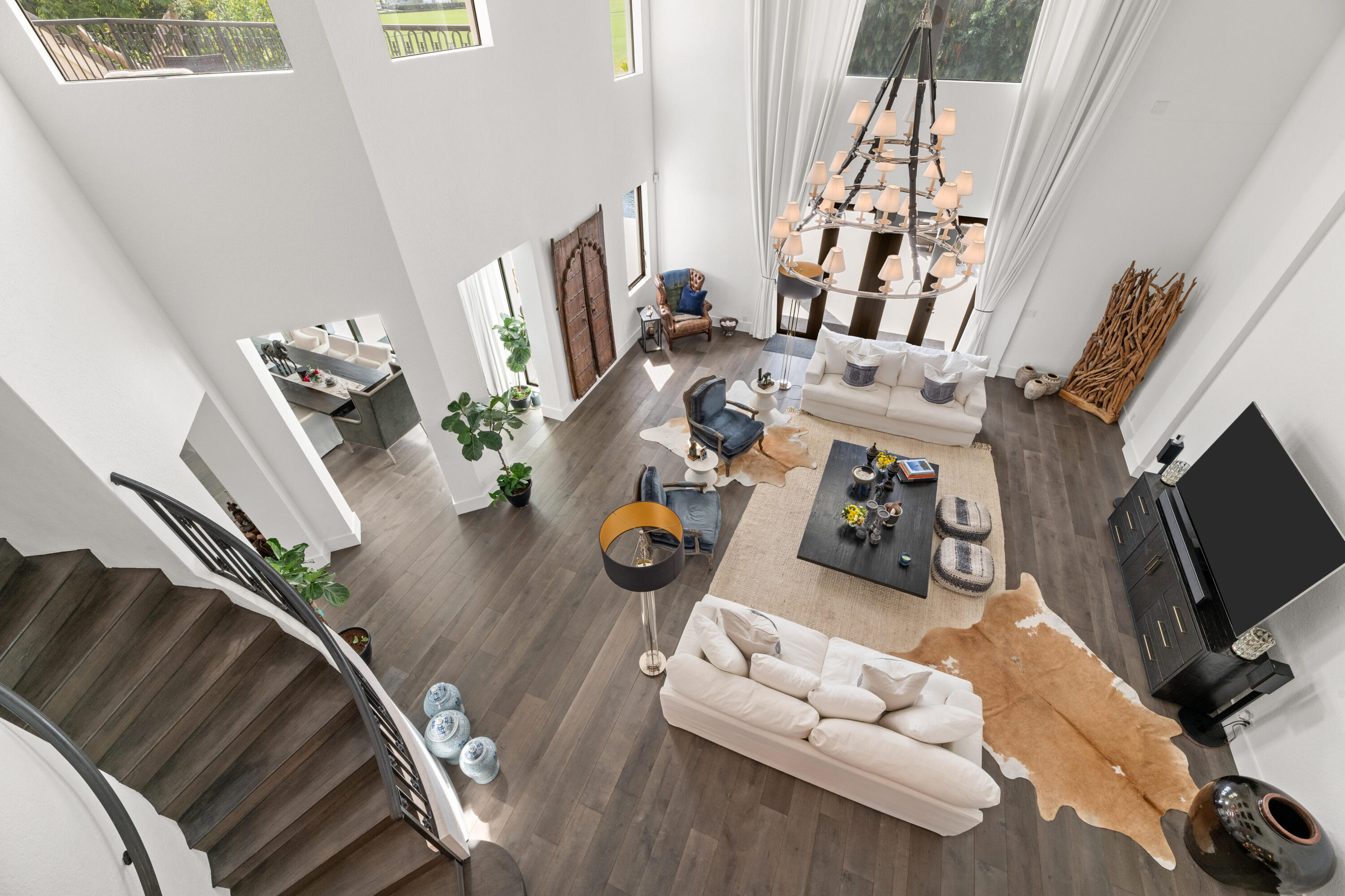Double-height living room with white sofas, a large chandelier, and a curved staircase.