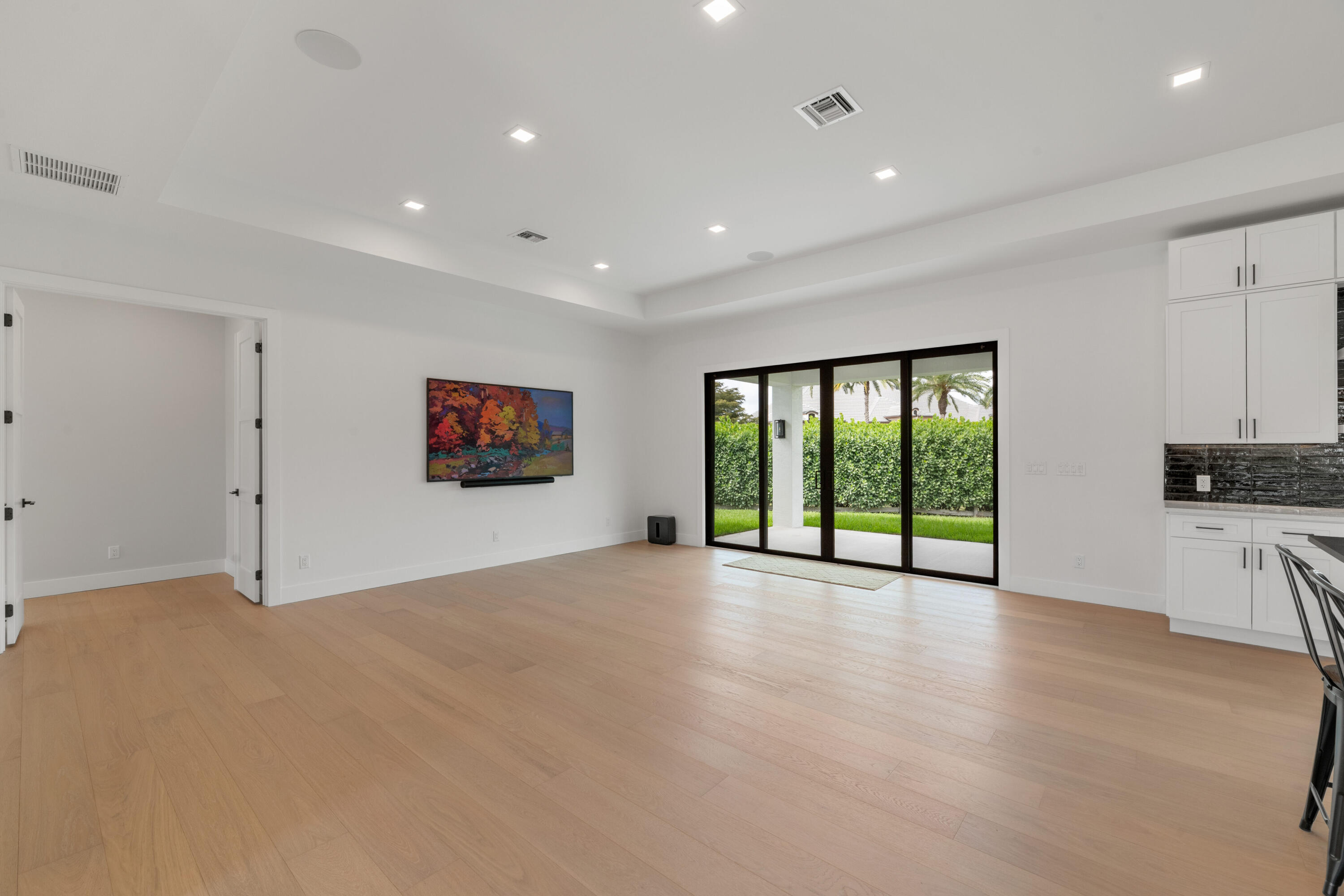 Open living room with light wood floors, sliding glass doors, and white kitchen cabinetry.