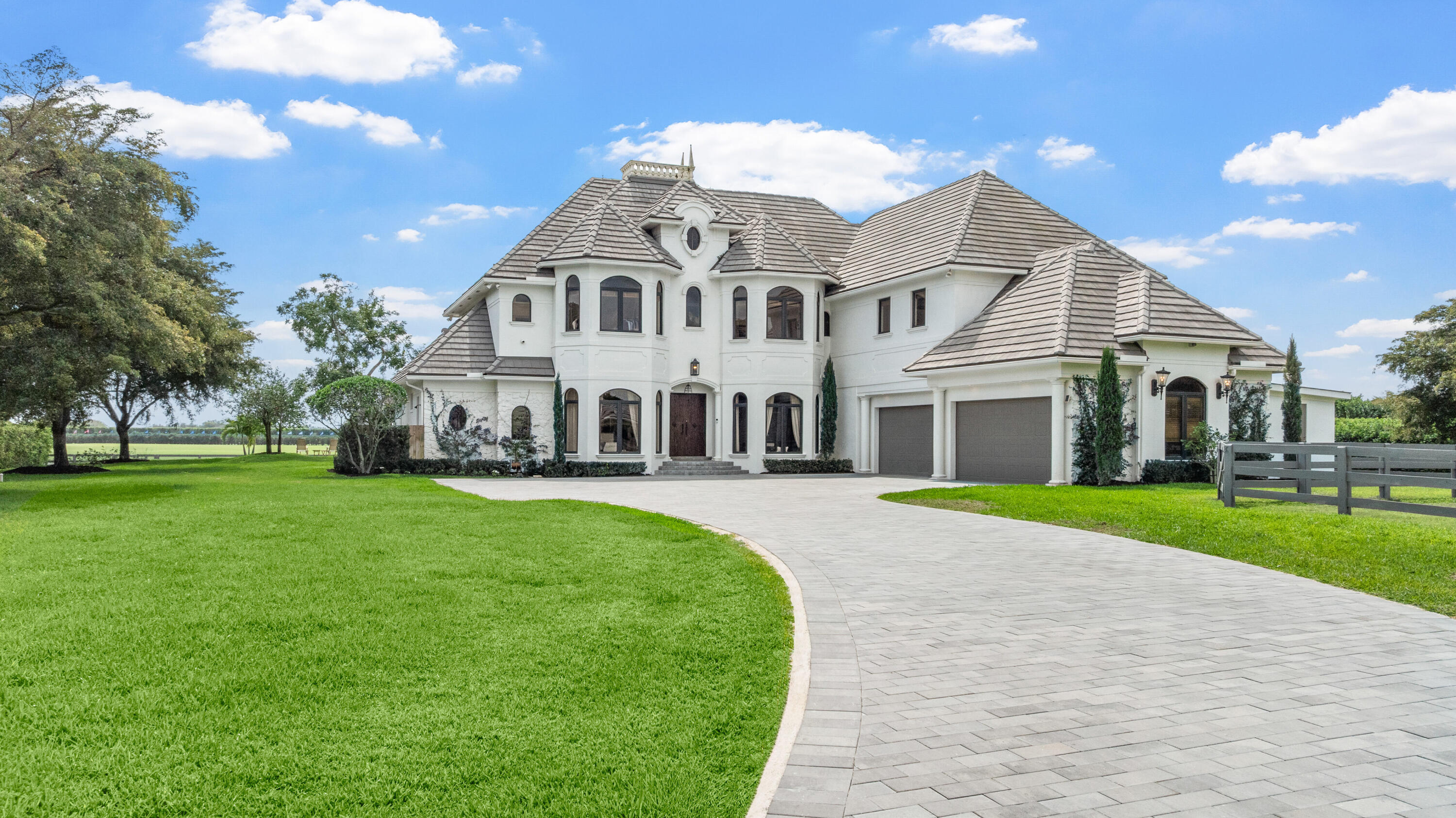 White two-story home with a gray tile roof, double garage, and curved paved driveway.