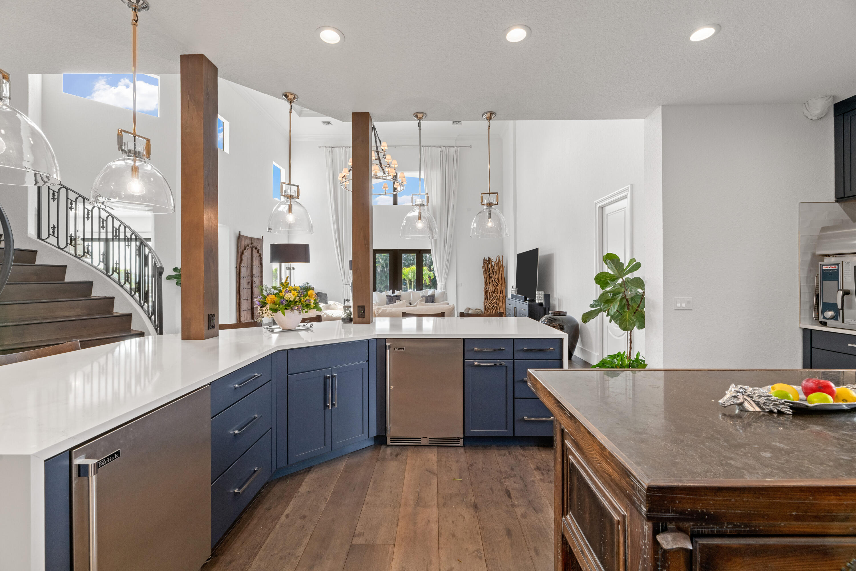 Open kitchen with navy cabinets, white counters, a wood island, and a curved staircase.