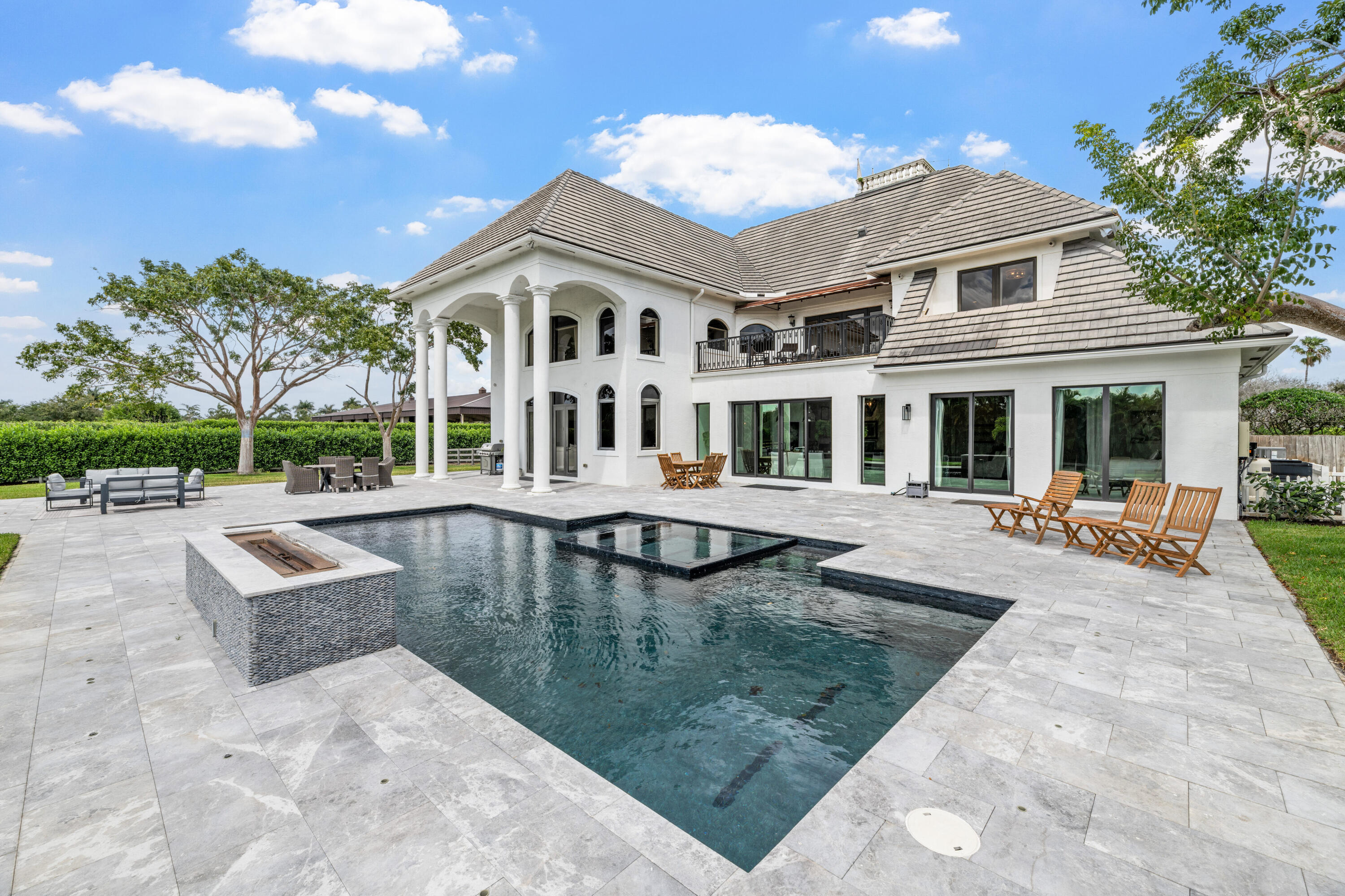 White two-story home behind a geometric pool and raised spa on a stone patio.