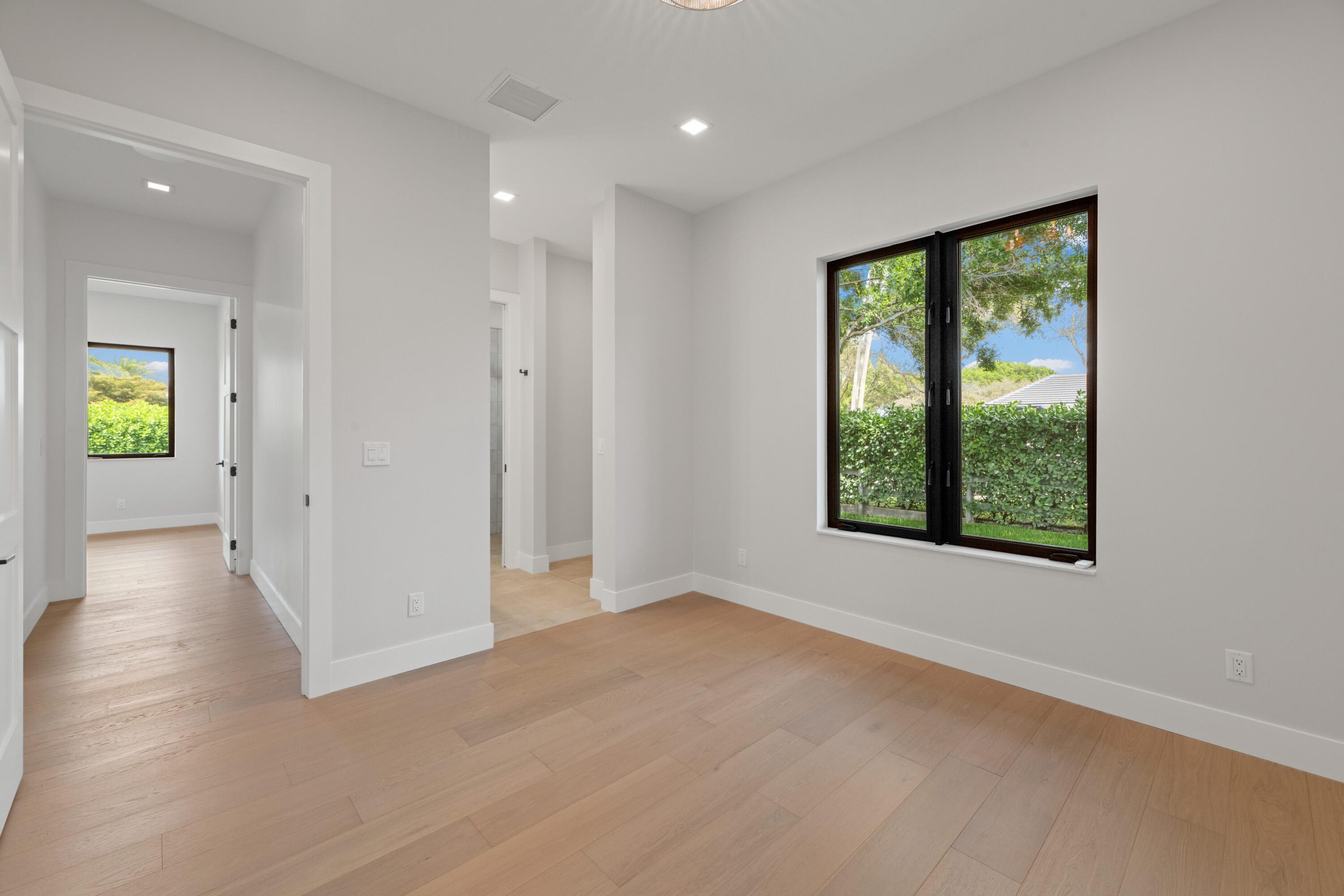 Unfurnished room with light wood floors and a large black-framed window overlooking greenery.