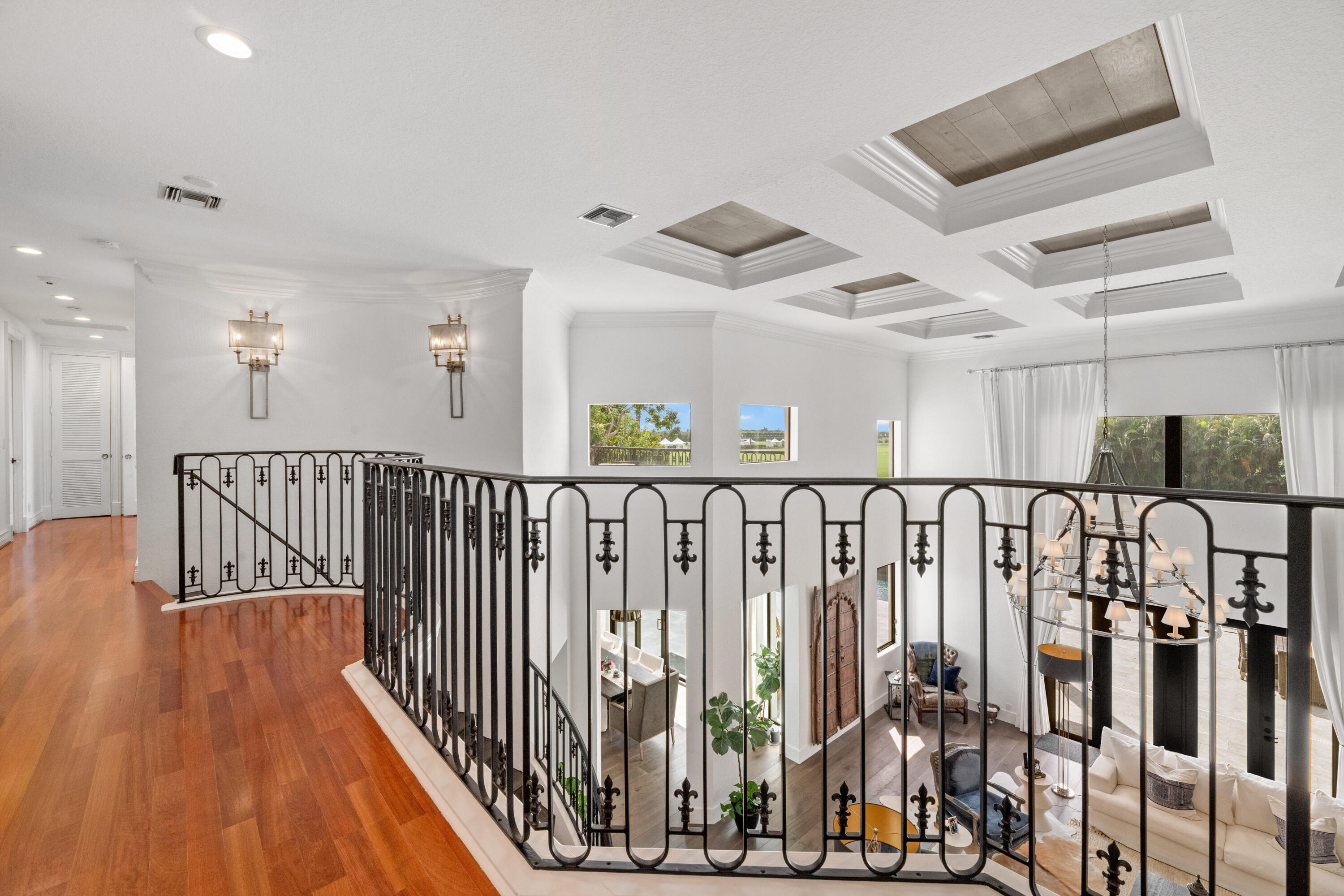 Second-floor landing overlooking a living room, with polished wood floors and an ornate black iron railing.